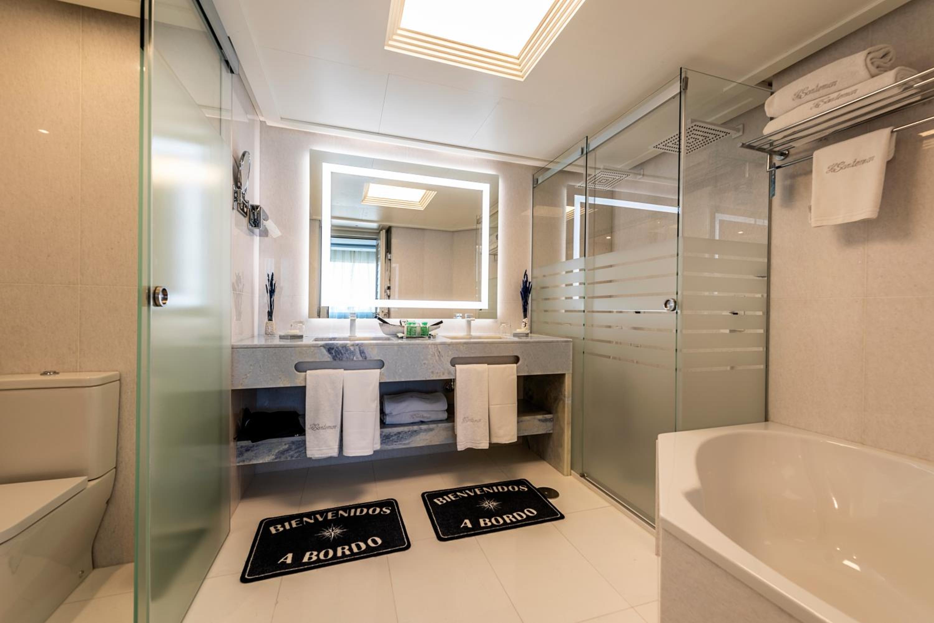 A bathroom with a marble vanity, backlit mirror, glass walk-in shower, and a soaking tub.
