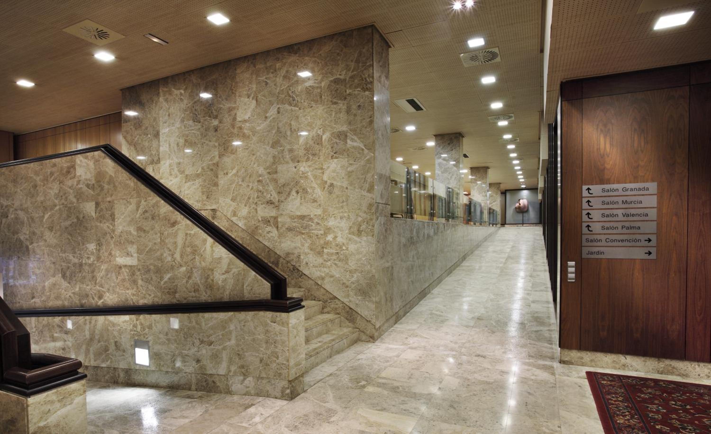 A wide corridor with polished beige marble walls and flooring, a ramp, stairs, and wooden wall panels.