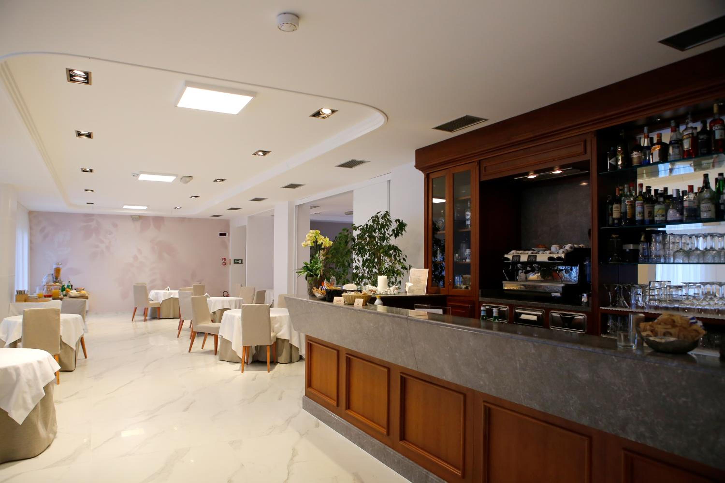A dining room and bar area with a stone counter, dark wood shelving, white marble floors, and draped tables.