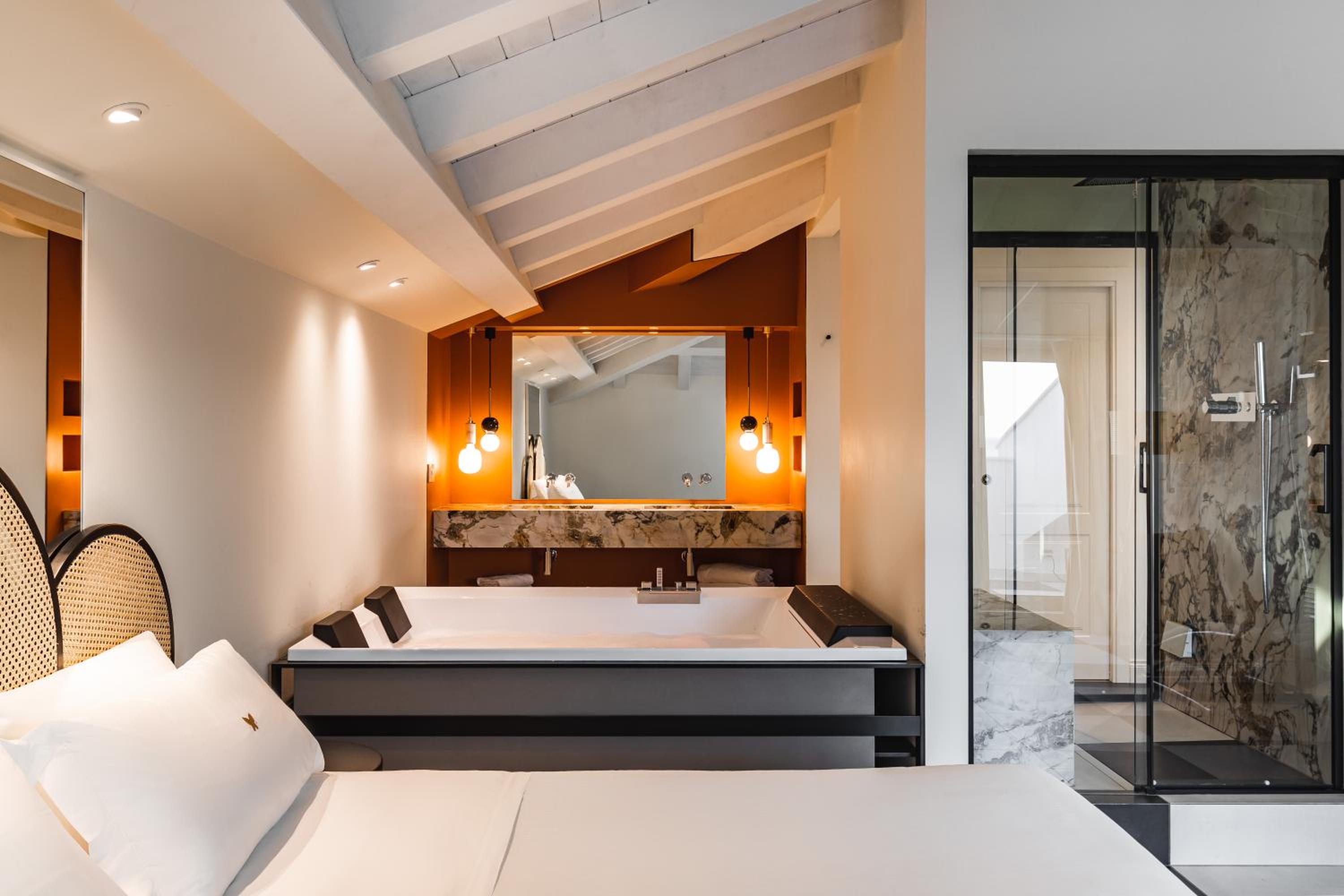 A guest room with a large bathtub under an angled beamed ceiling, featuring a marble vanity and glass shower.