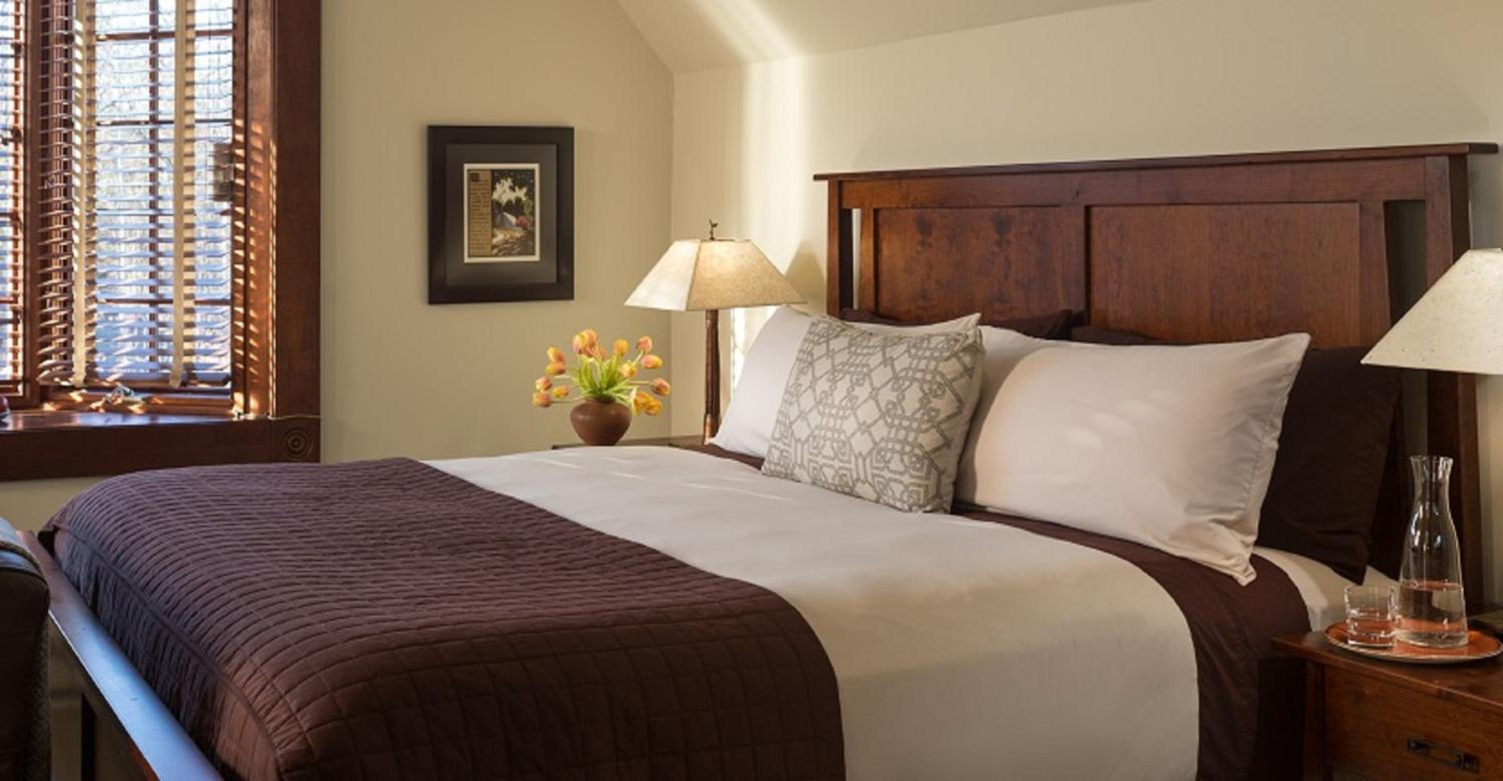 Bedroom featuring a dark wood headboard, quilted brown runner, bedside lamps, and a window with wooden blinds.