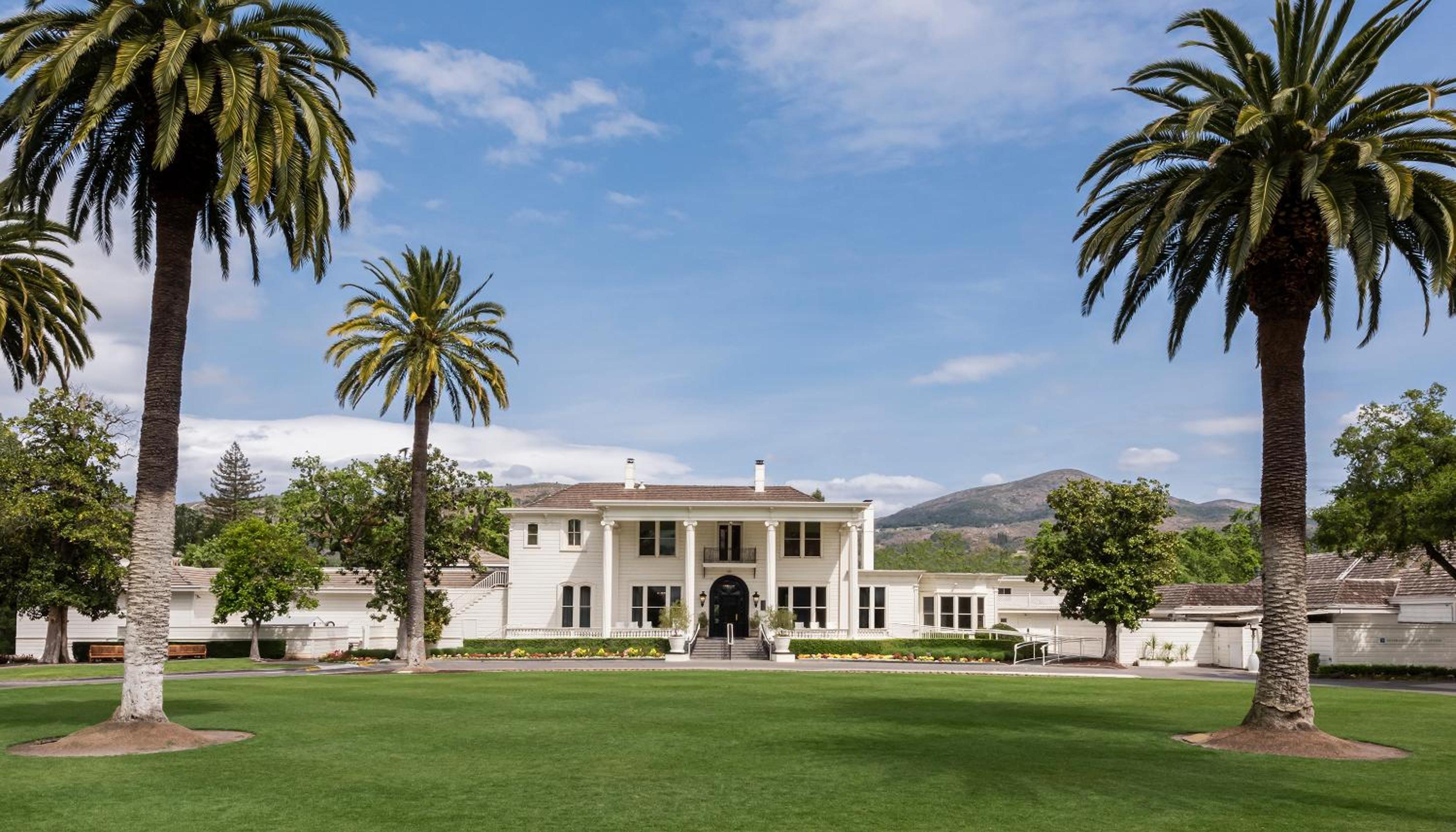 The white mansion facade at Silverado Resort stands beyond a broad green lawn framed by tall palm trees.