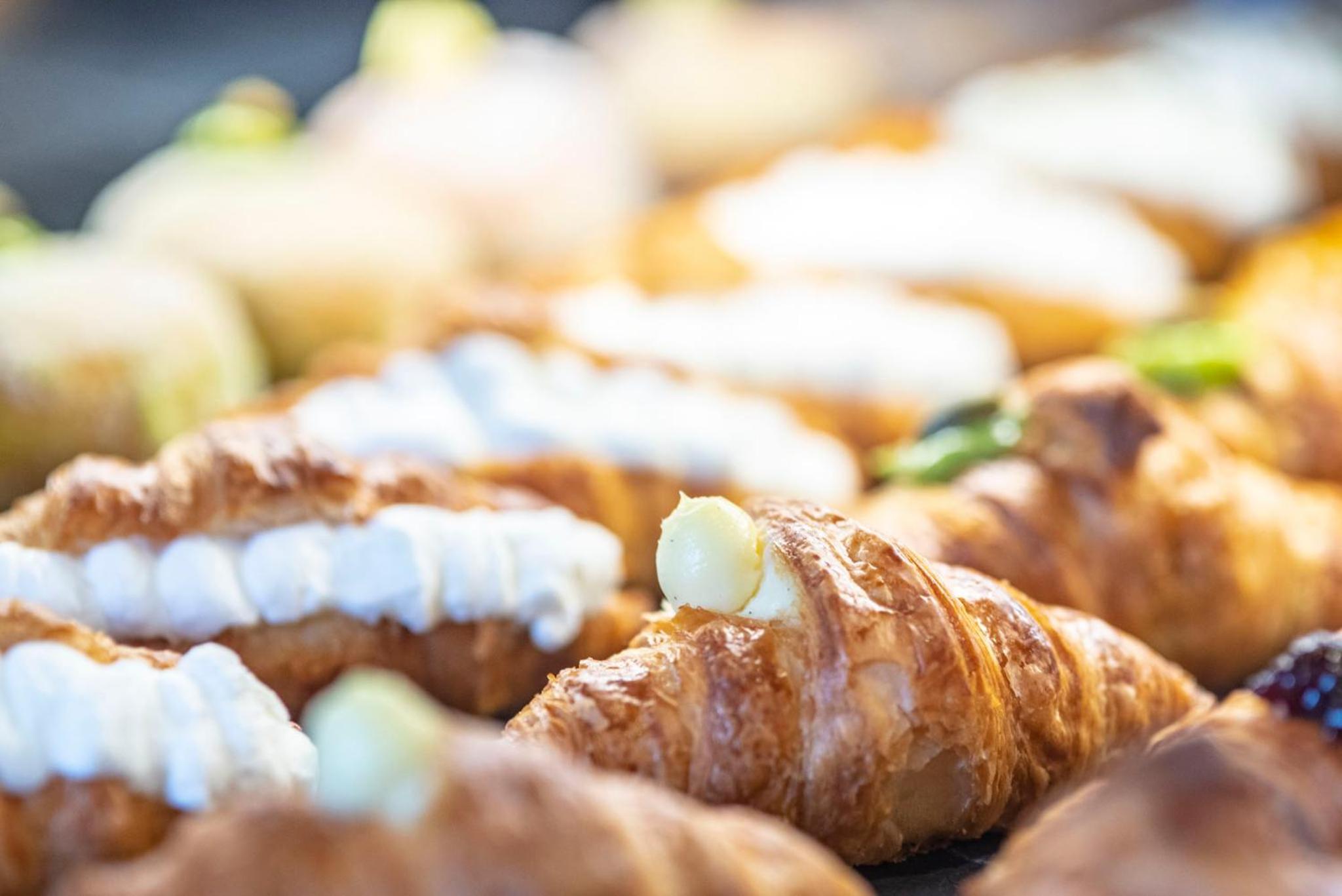 Rows of croissants filled with piped white cream and pastry cream on display.