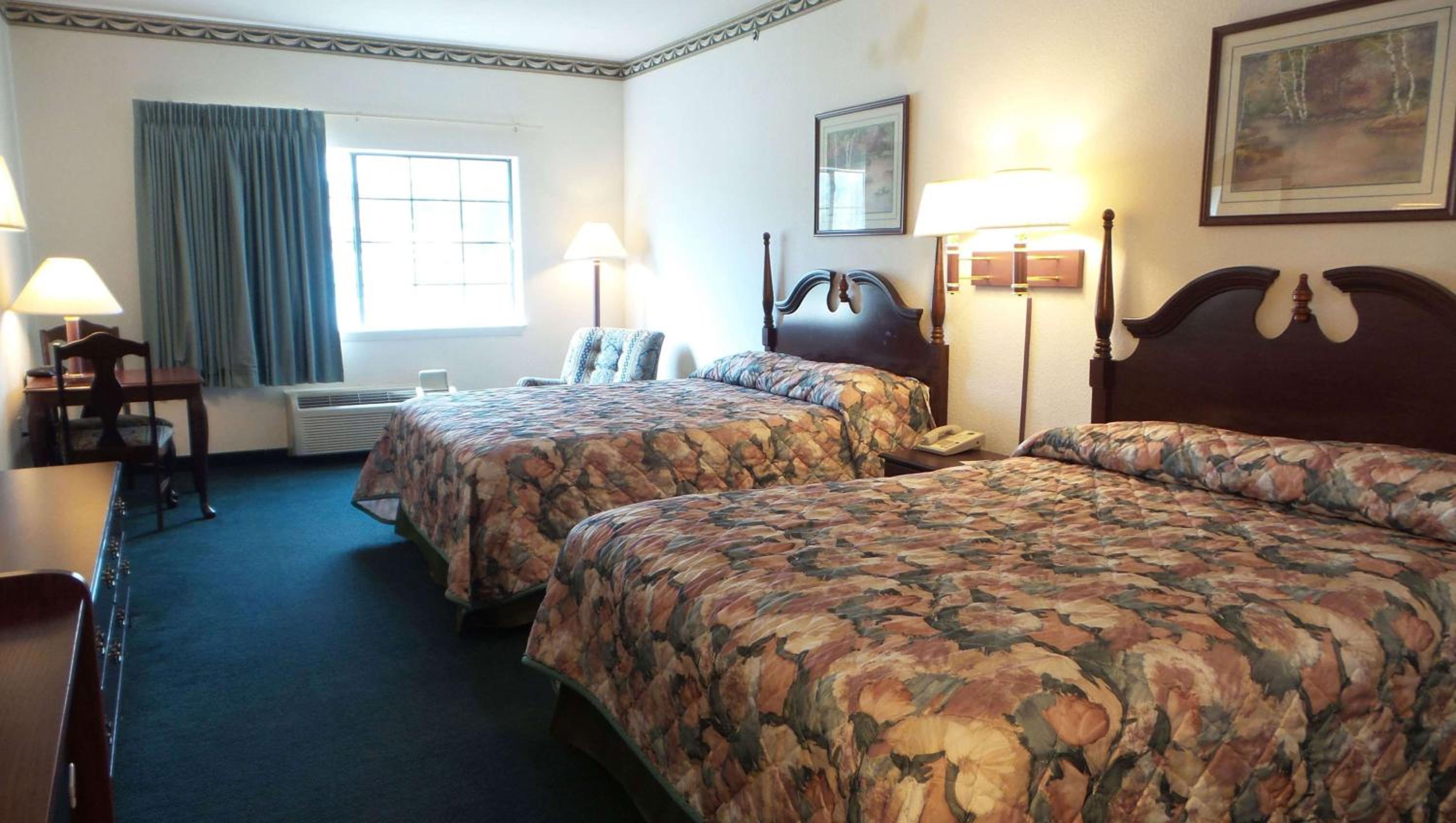 A hotel bedroom with patterned floral bedspreads, dark wood furniture, and carpeted flooring.