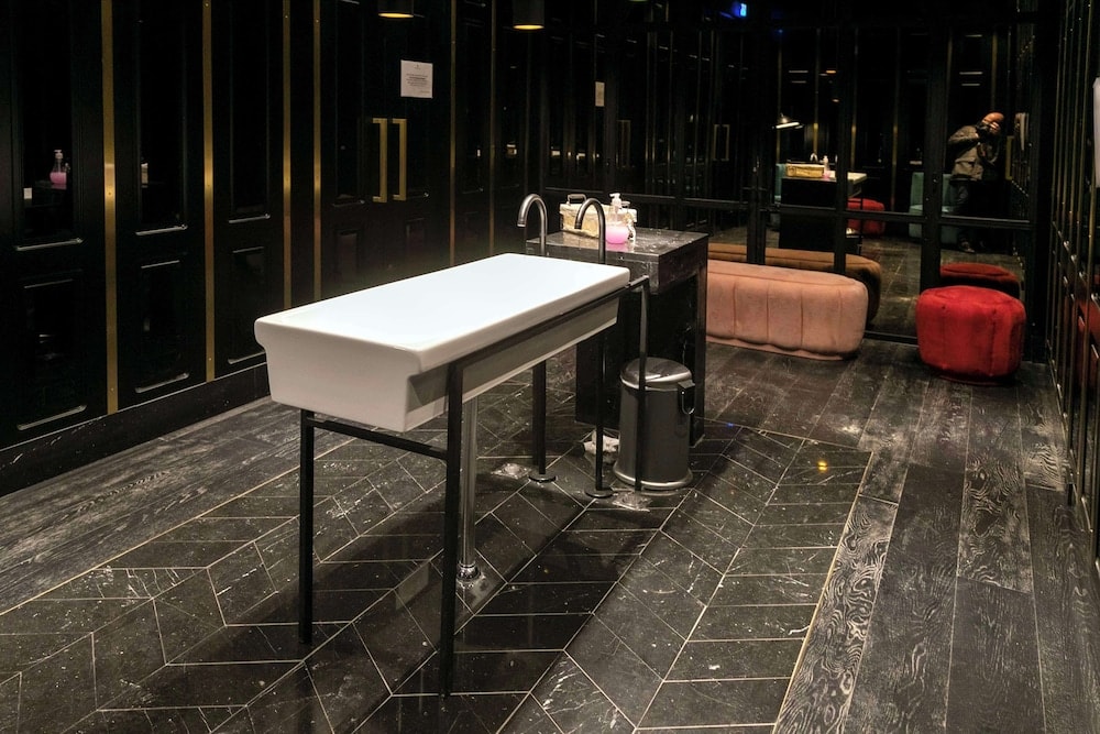 Restroom with dark wood-grain chevron tile floors, black paneled walls, and a white trough sink on metal legs.
