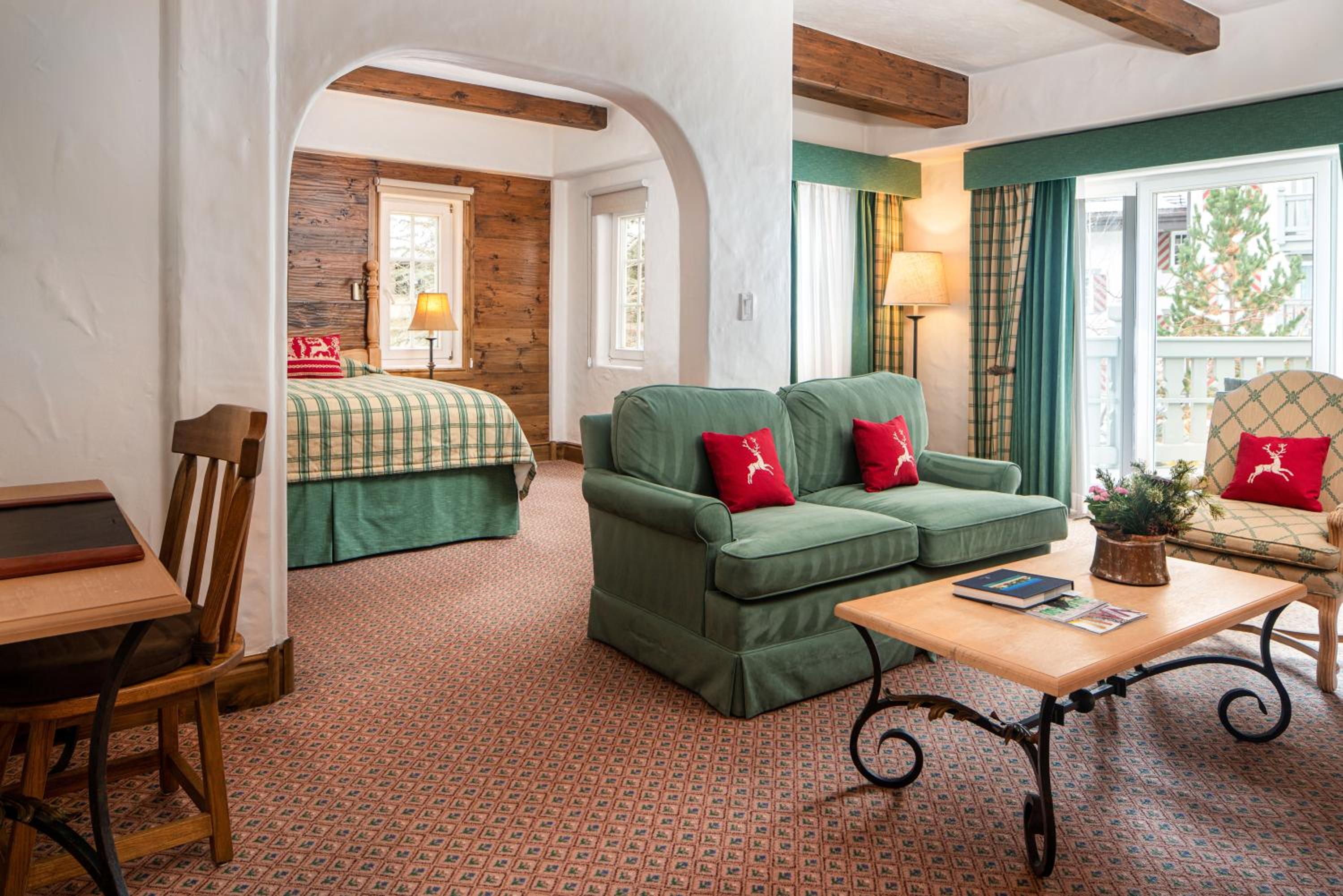 Hotel suite with an arched doorway leading to a bed, a green sofa, and exposed wood ceiling beams.