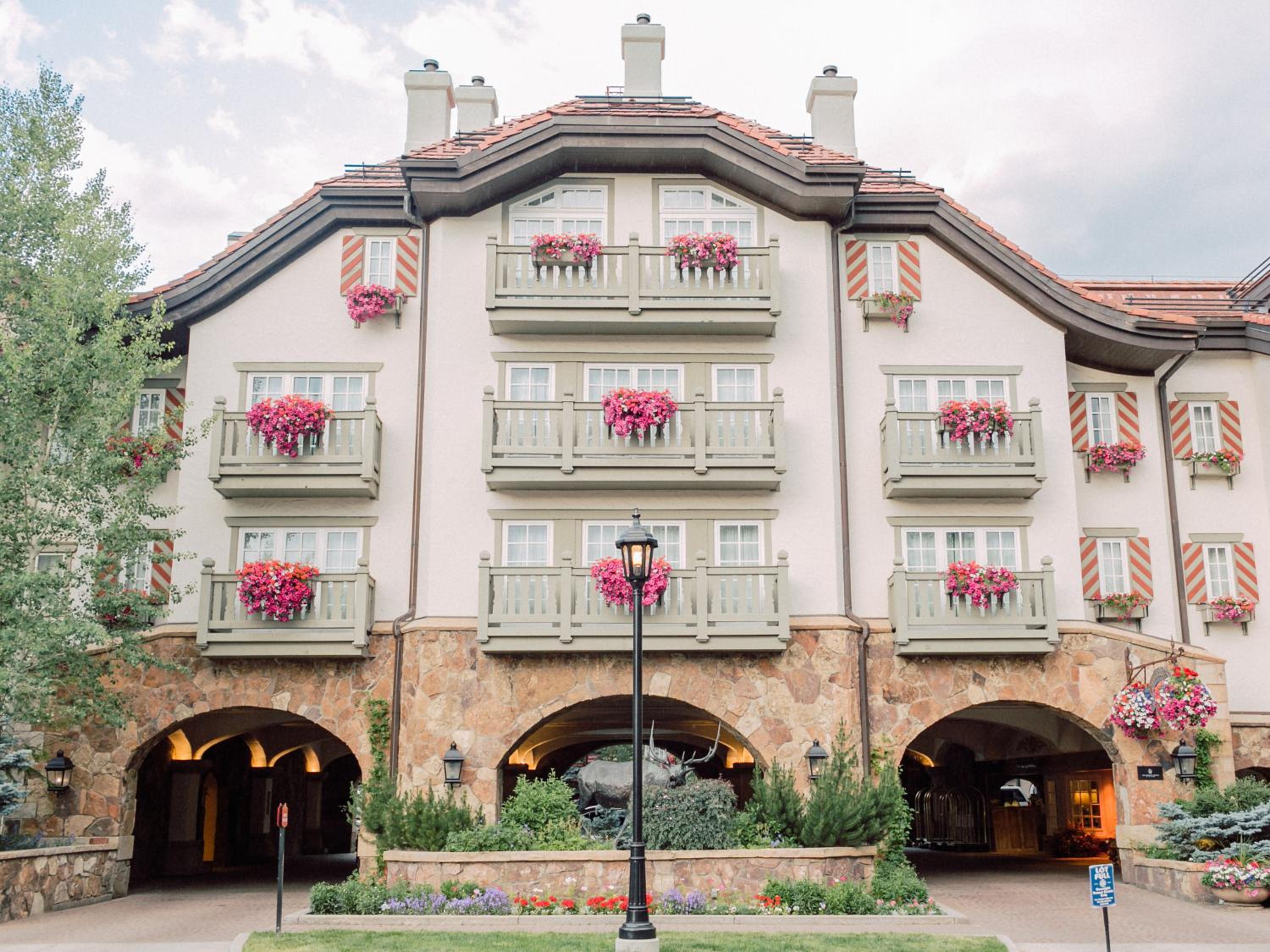 Hotel facade with stone ground-floor arches and upper balconies trimmed with overflowing pink flower boxes.