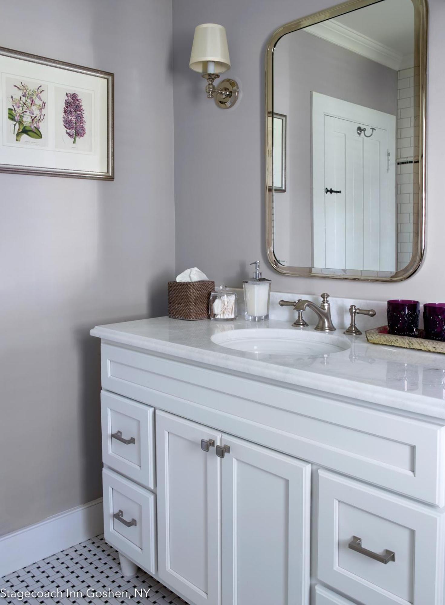 A bathroom vanity with a white marble top, polished metal faucet, rounded mirror, and tiled floor.
