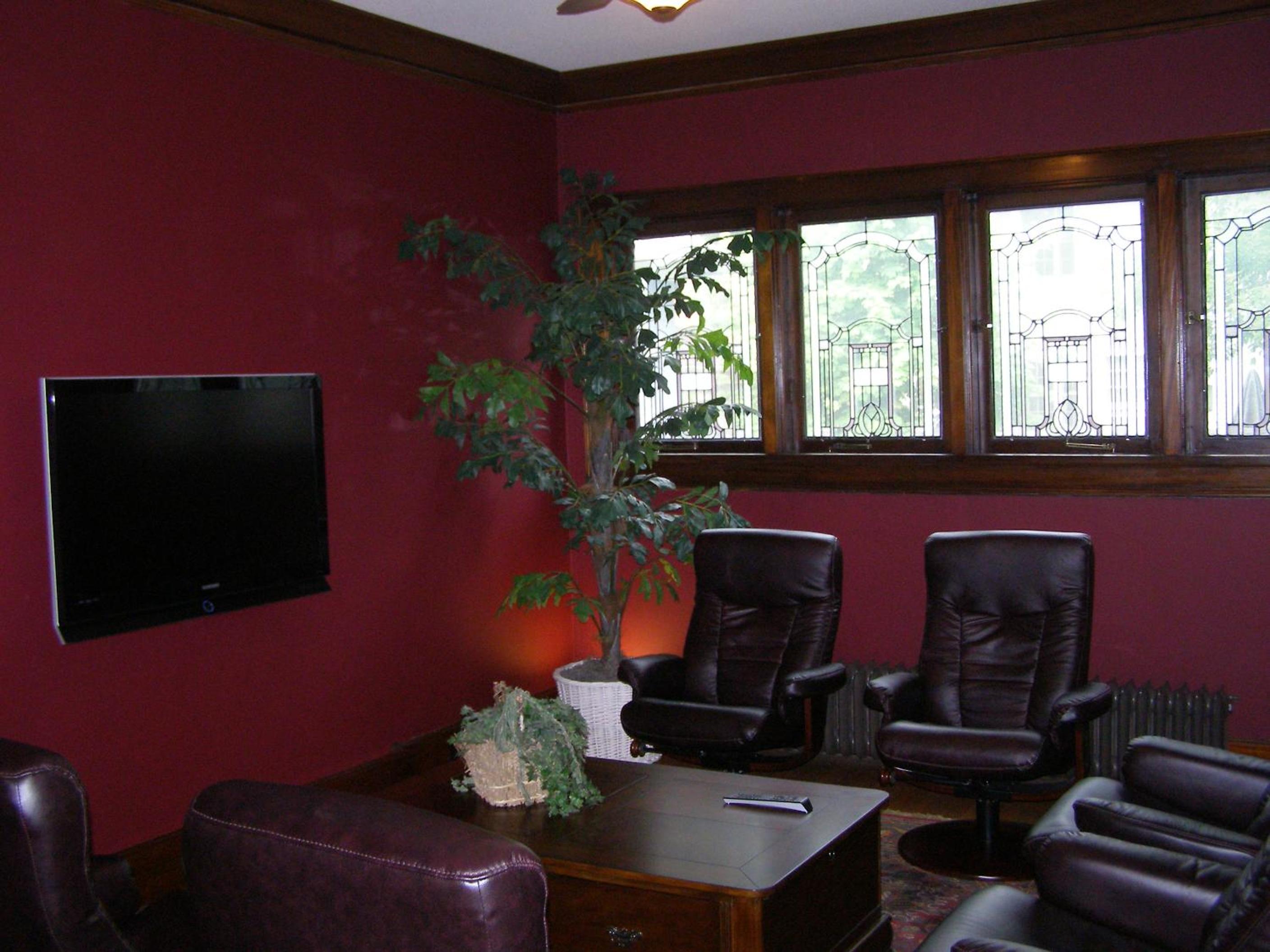 A sitting room with red walls, leather armchairs, a coffee table, and decorative stained-glass windows.