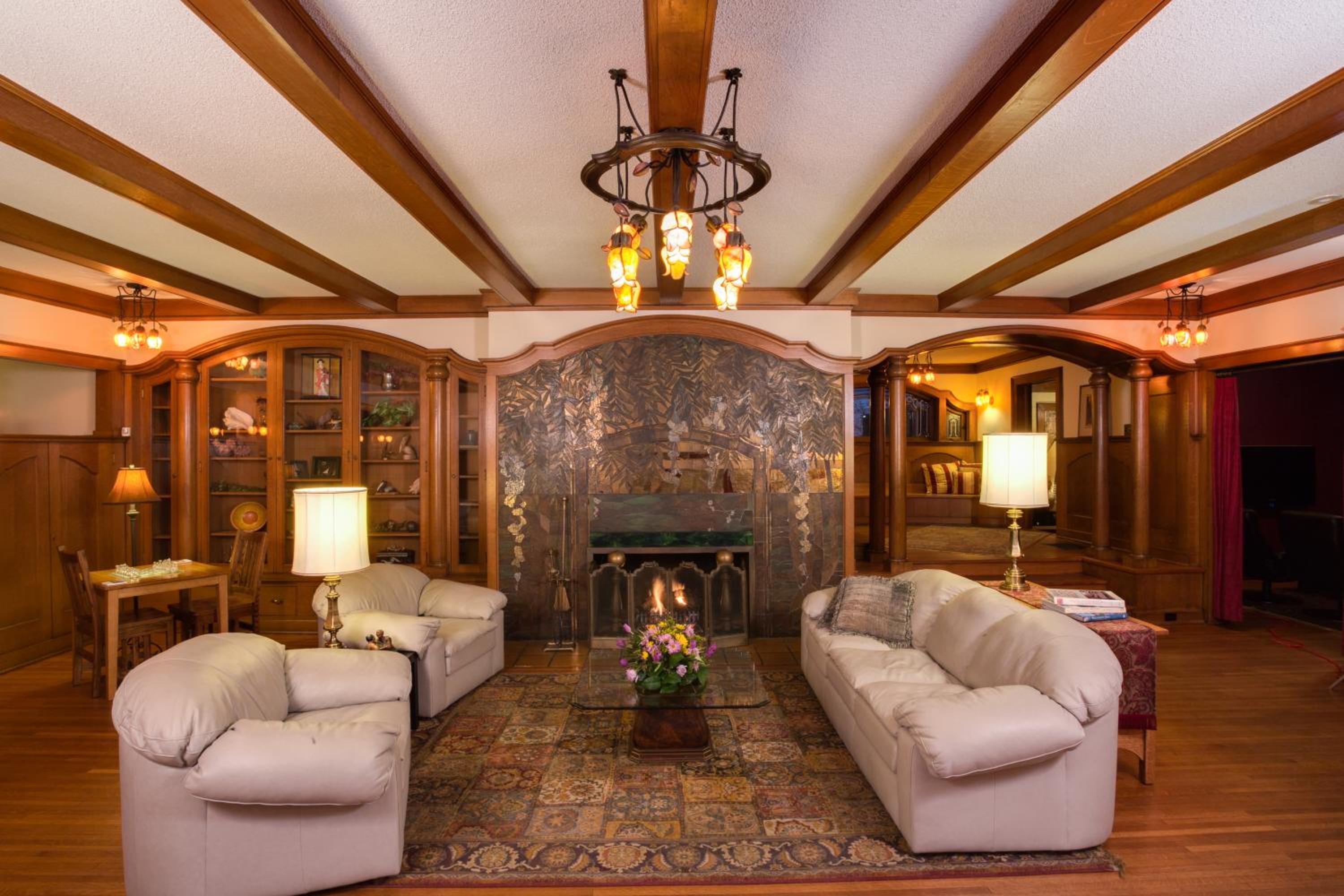 A living room featuring beamed ceilings, a fireplace with a decorative hood, and plush light sofas.