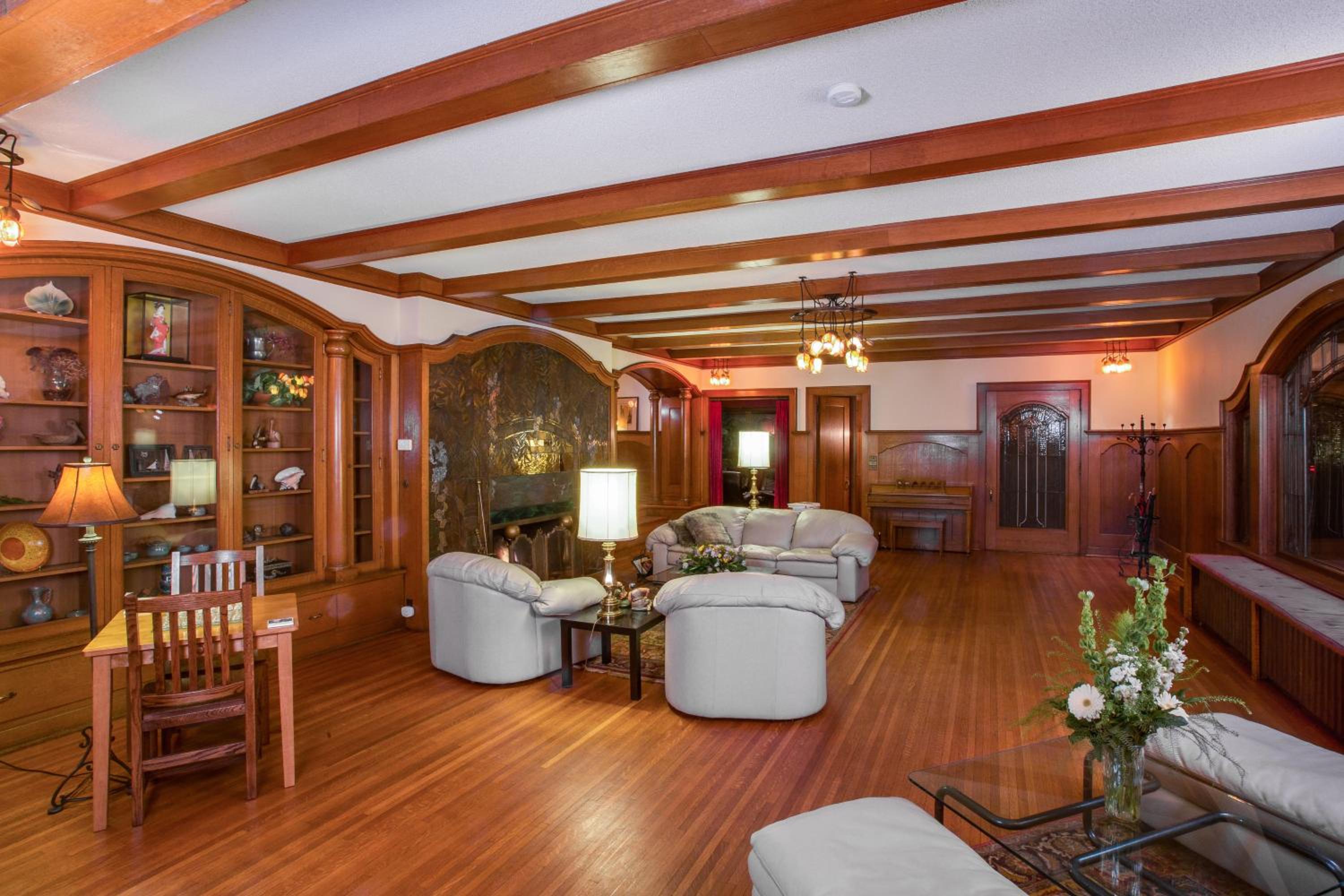 Living area with polished hardwood floors, beamed ceilings, built-in display cabinets, and seating.