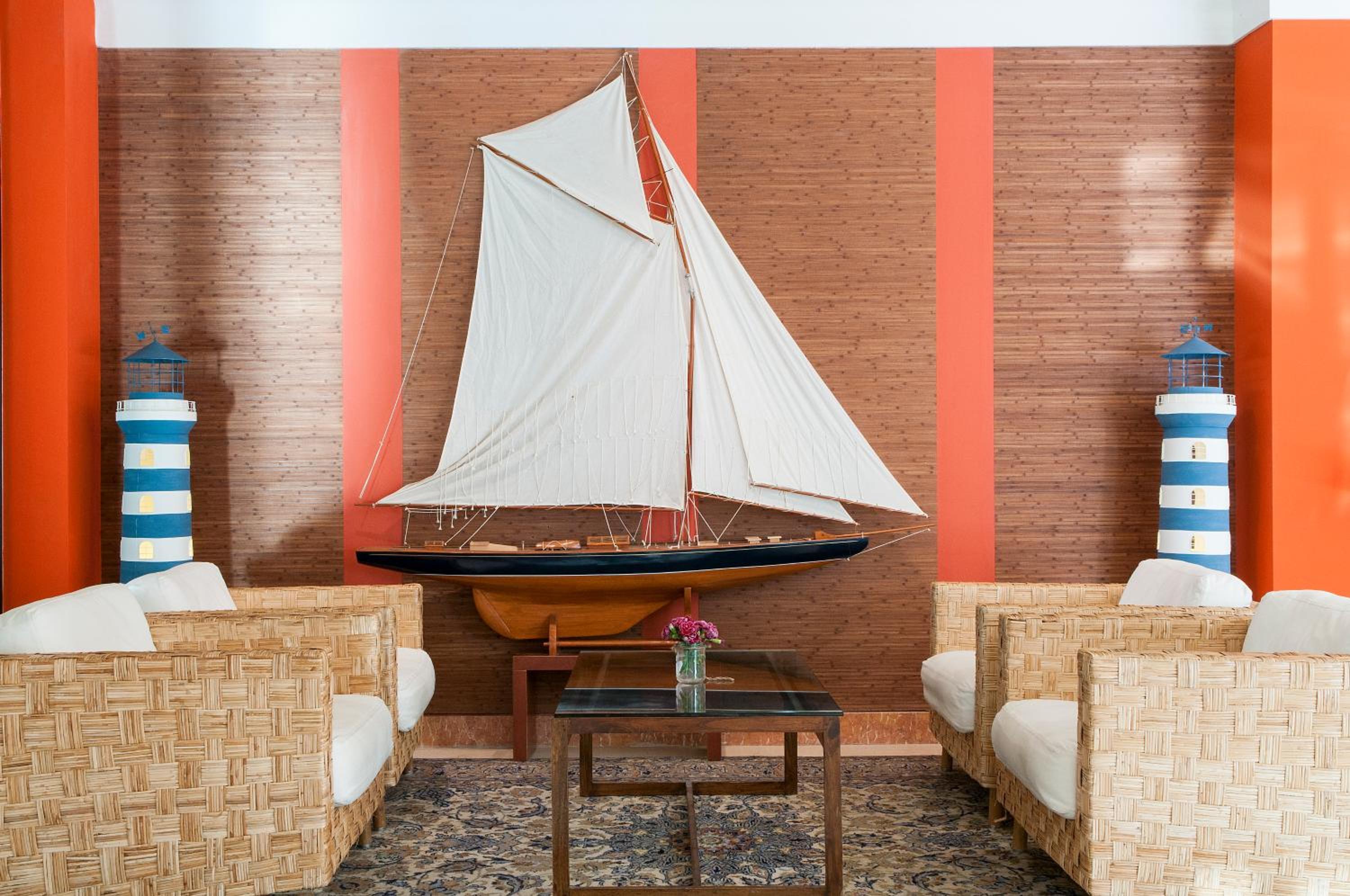 A seating area with woven armchairs, a glass coffee table, and a model sailboat mounted on the wall.