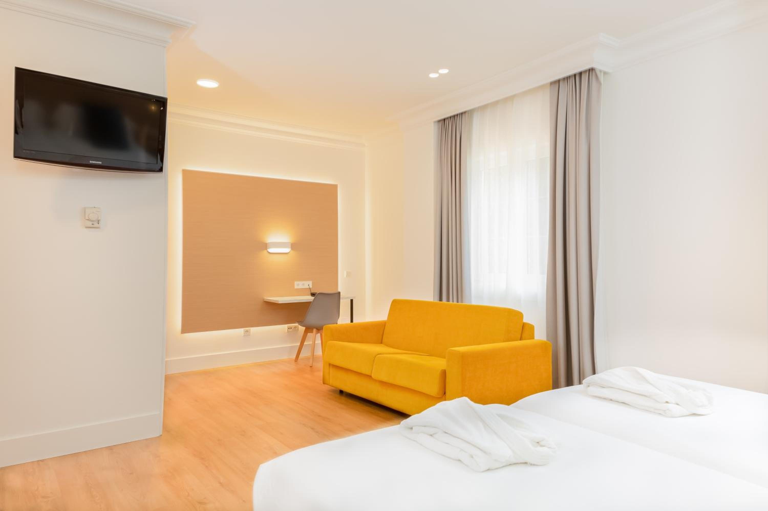 A hotel room featuring a mustard sofa, work desk, and beds dressed in white linens.