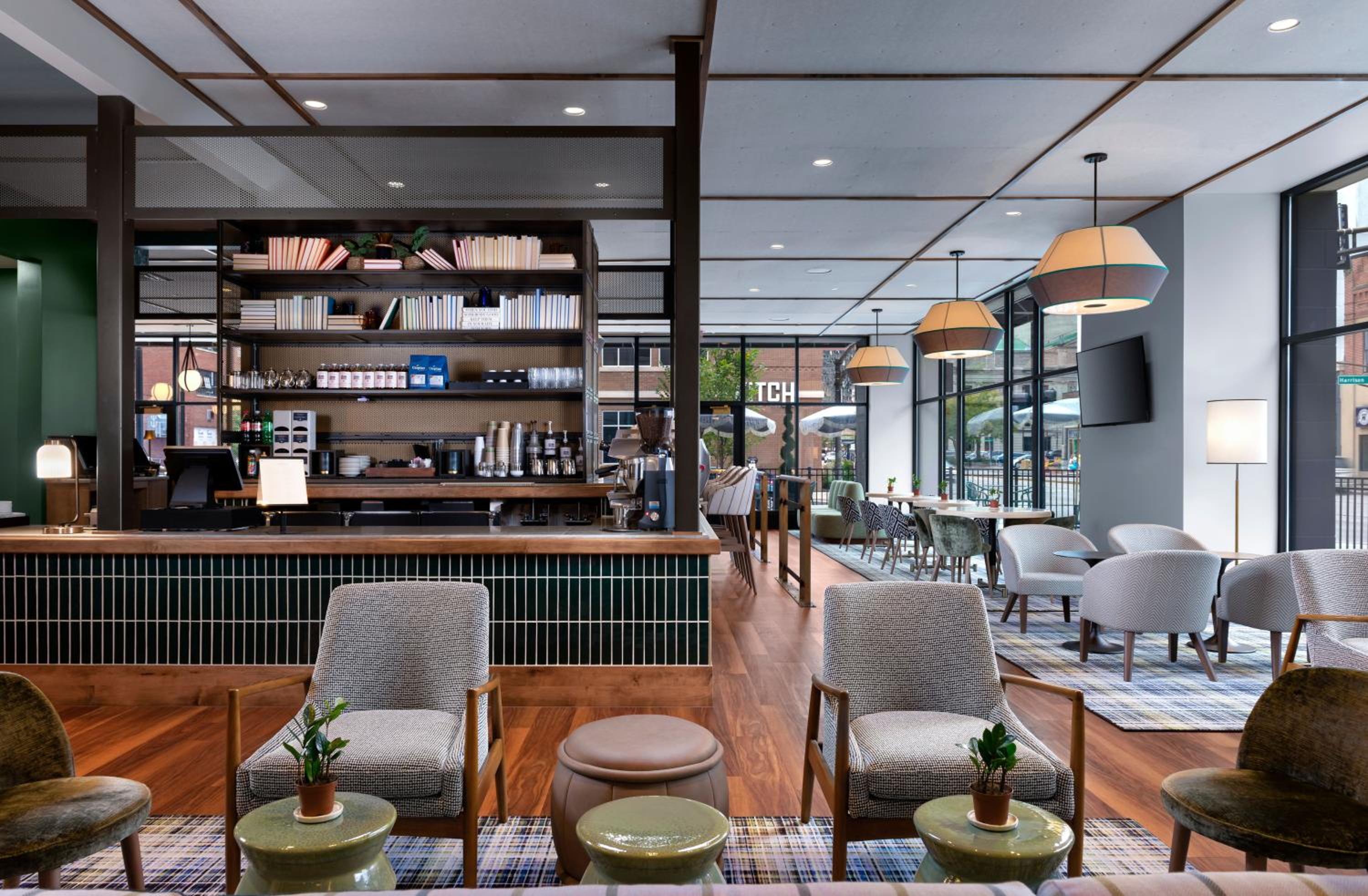 Lounge and bar area with tiled counter, mid-century modern chairs, low tables, and large street-facing windows.