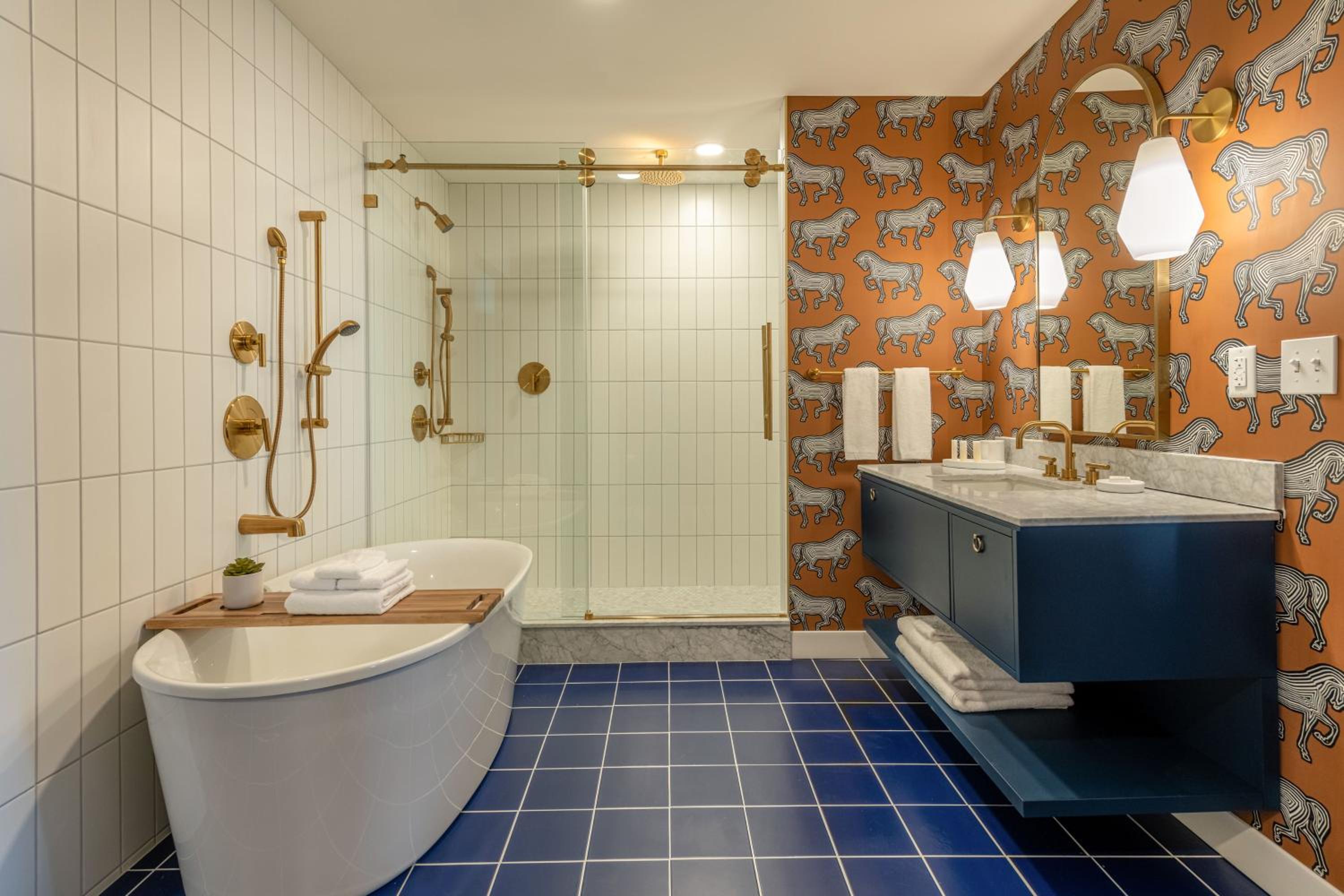 Bathroom featuring a standalone tub, glass-enclosed shower, brass fixtures, blue tile floor, and animal wallpaper.