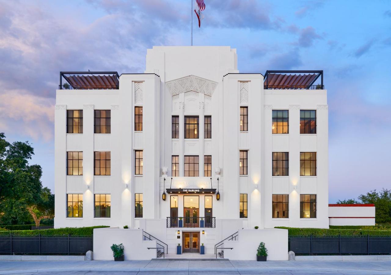 Exterior facade of The Darling, a white Art Deco building with lit windows and rooftop pergolas at dusk.