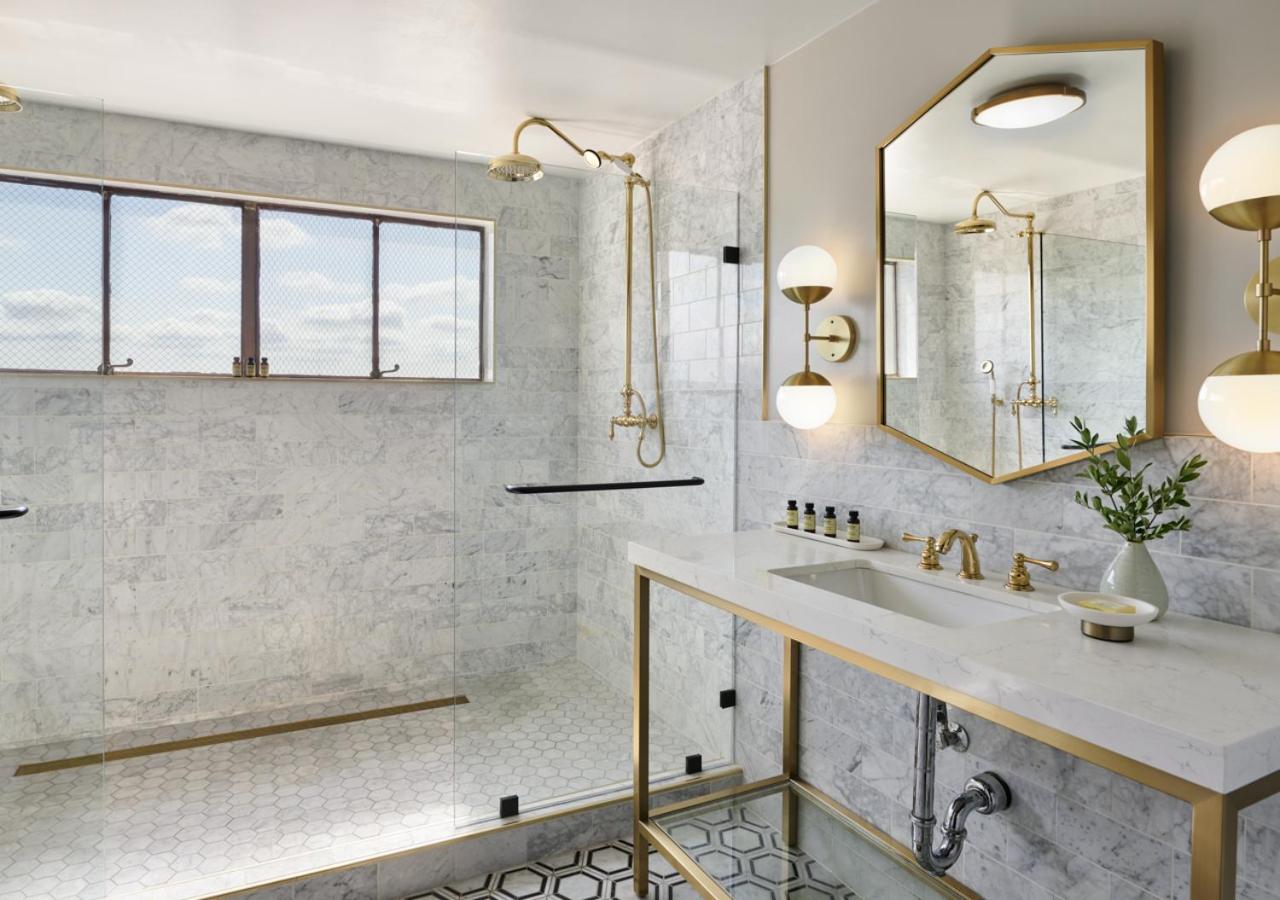 Marble bathroom with a glass-enclosed shower, brass fixtures, hexagon floor tiles, and a vanity counter.