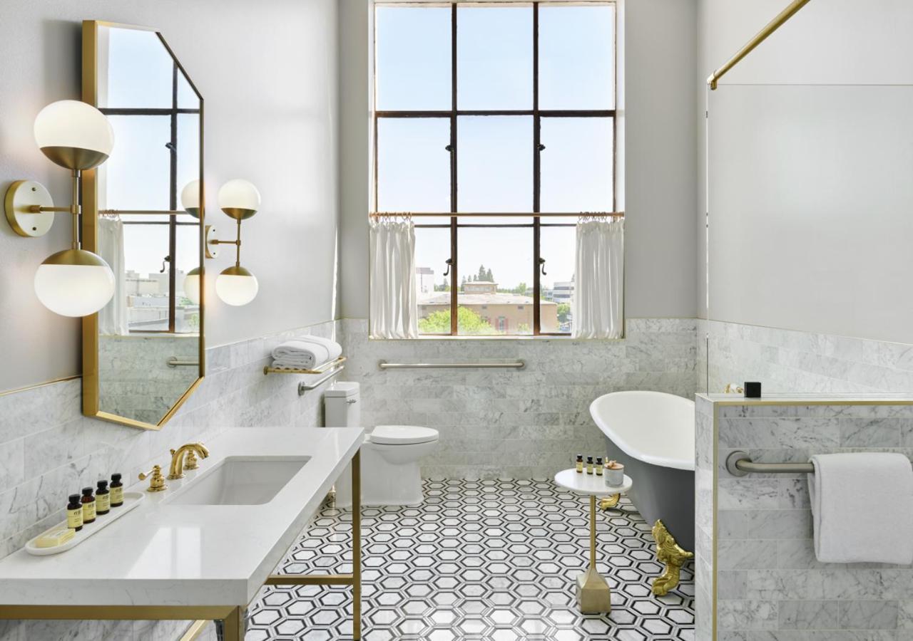 Bright bathroom featuring a clawfoot tub, marble walls, brass fixtures, patterned tile flooring, and a large window.