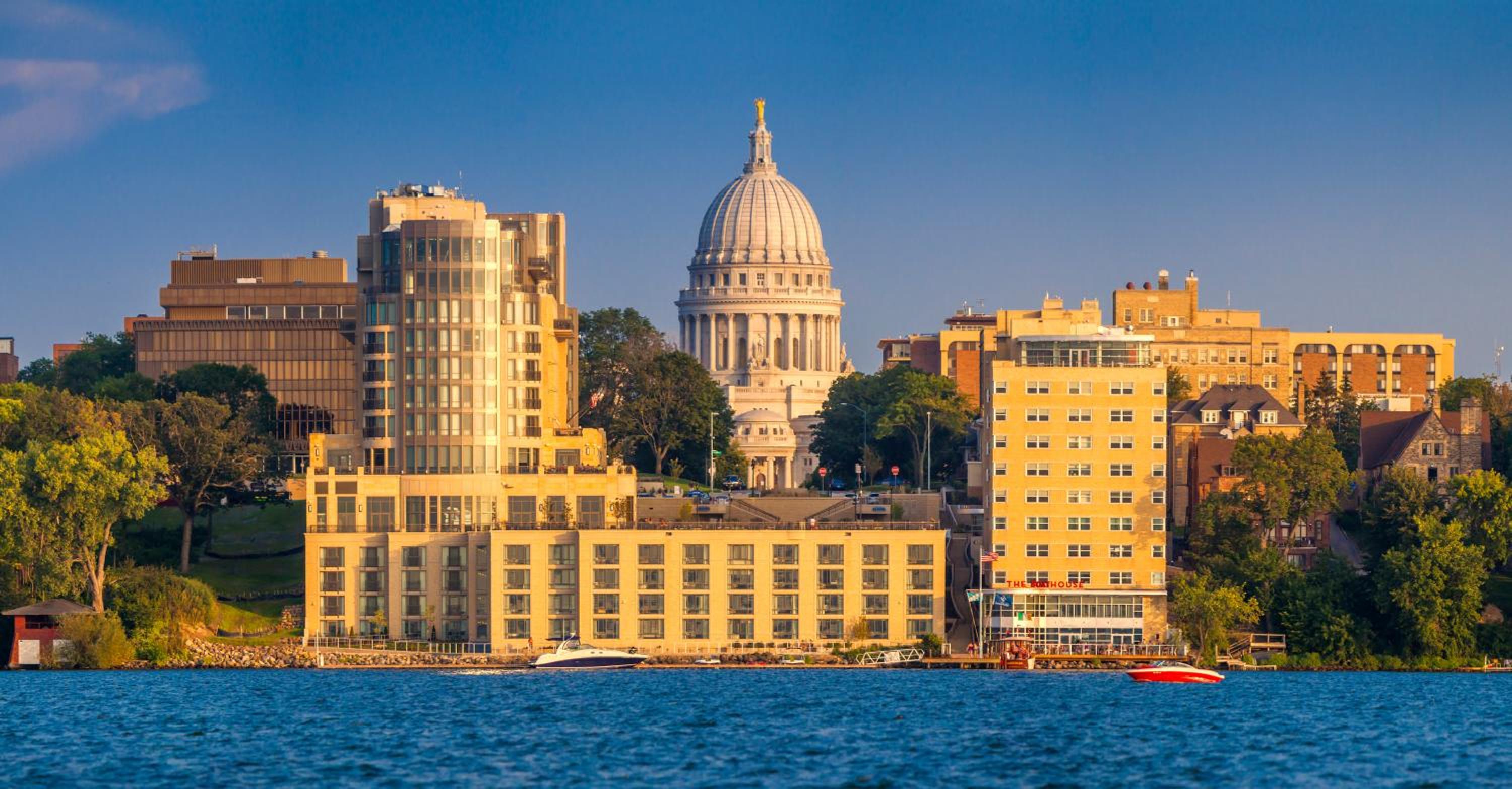 Lakefront facade of The Edgewater with city buildings and the Wisconsin State Capitol dome under a clear blue sky.