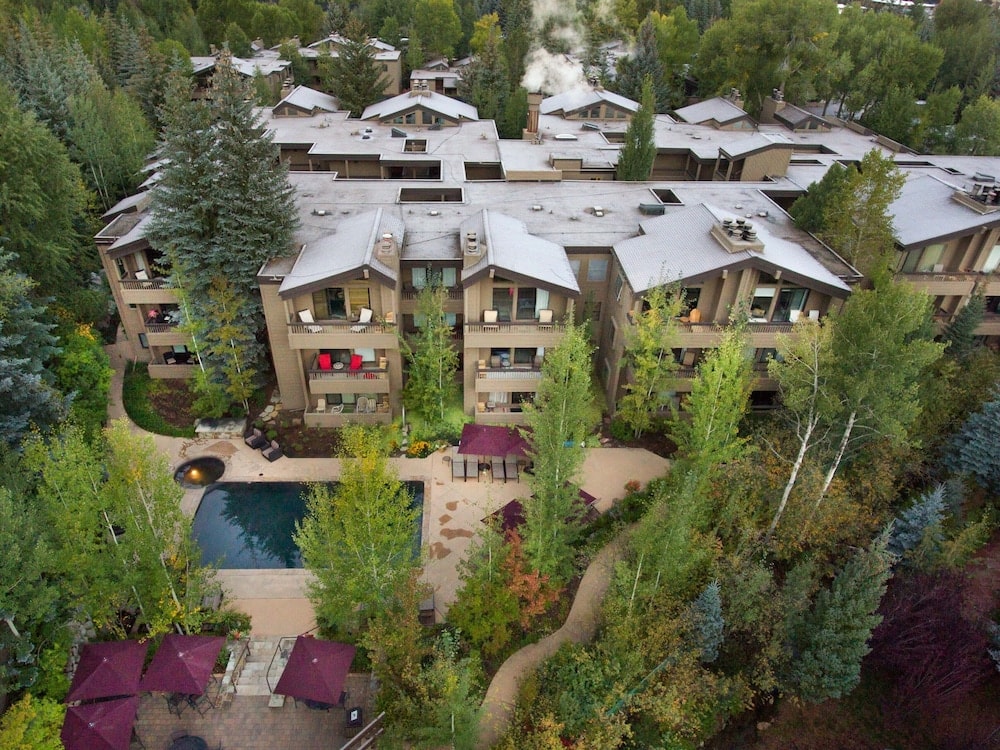Aerial view of multi-story timber buildings surrounding a pool patio set among dense pine and aspen trees.