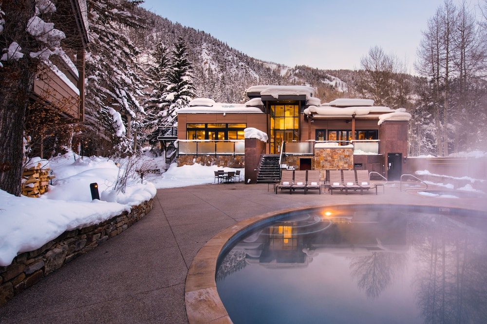 Steaming outdoor pool and lounge chairs on a snow-covered terrace fronting a lodge at The Gant.