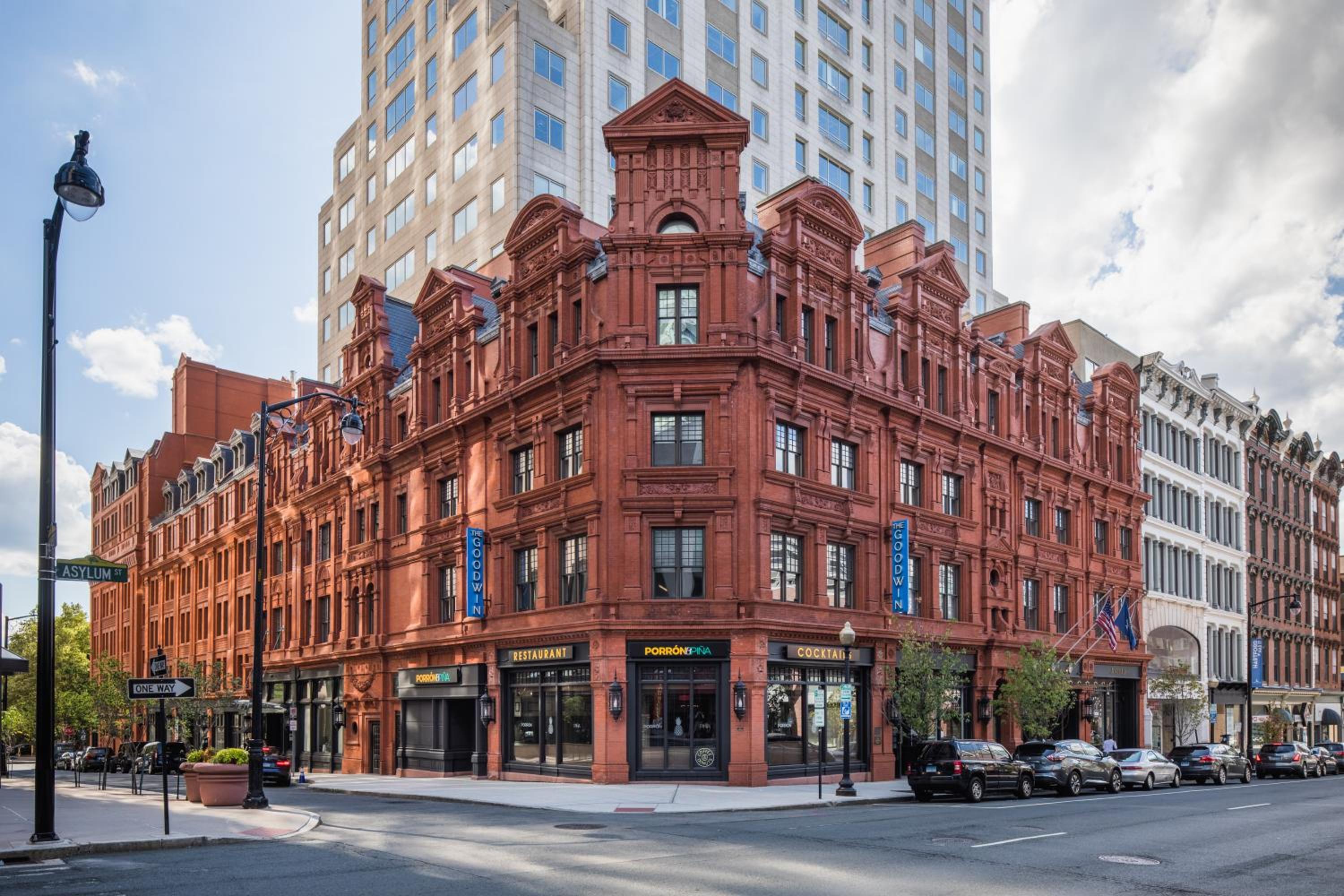 The red terracotta facade of The Goodwin stands on a city corner beneath a taller skyscraper.