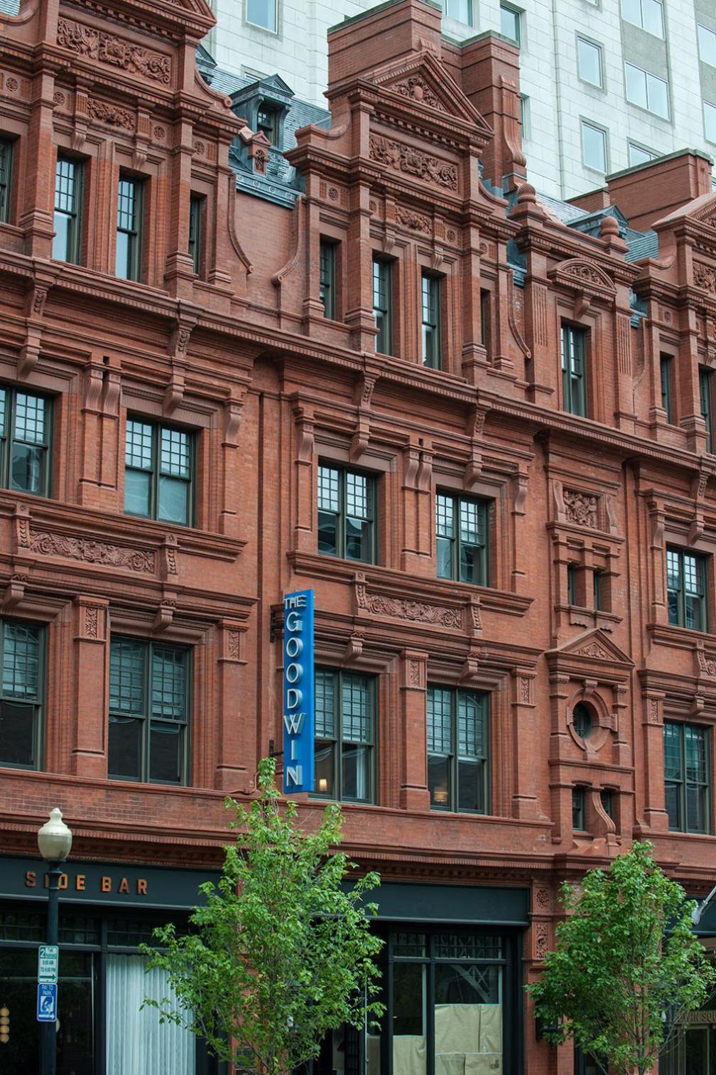 Detailed view of the red terracotta brick facade with decorative window surrounds and a blue vertical sign.