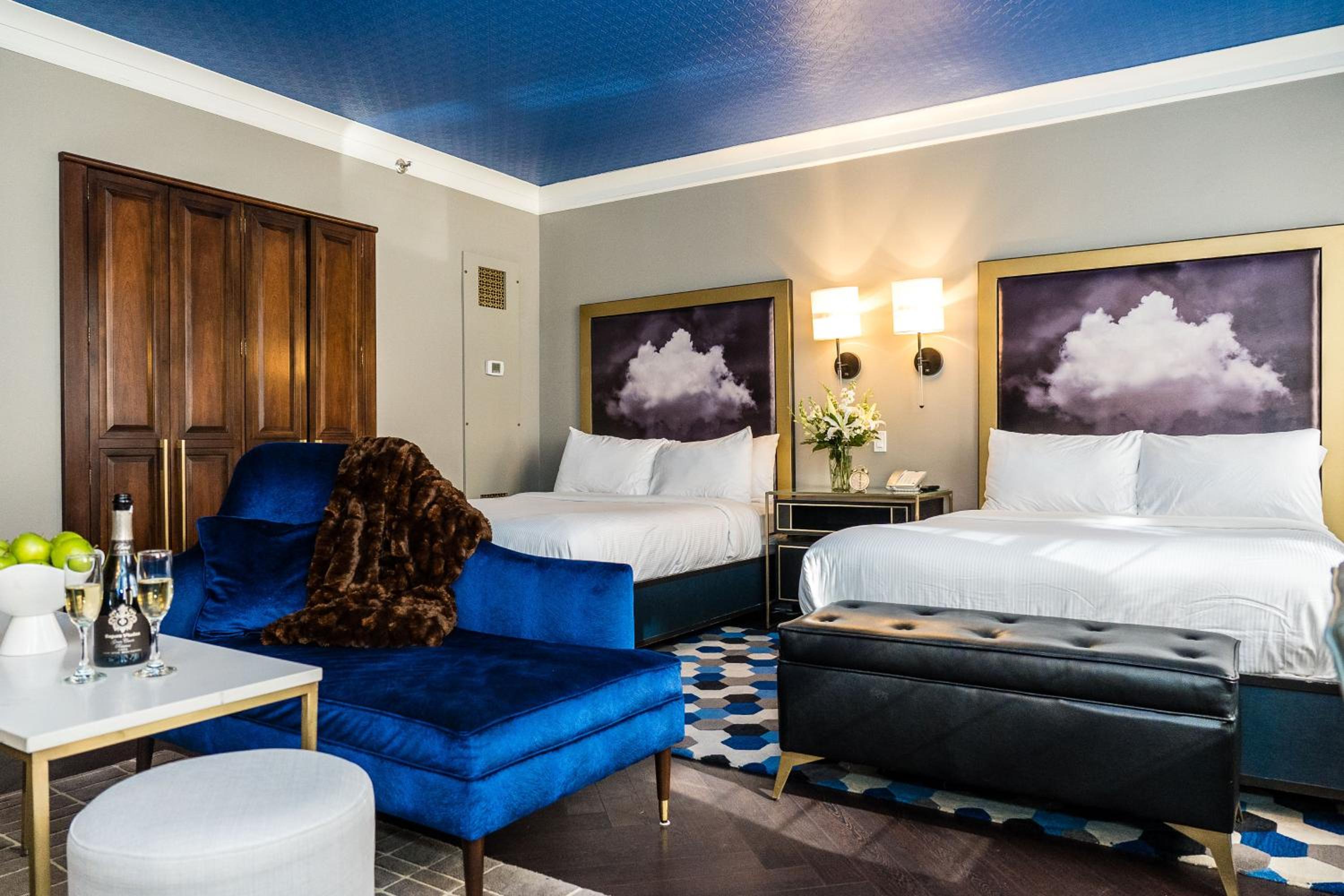 A guest room with a cobalt blue ceiling, dark wood floor, beds with cloud-print headboards, and a velvet chaise.