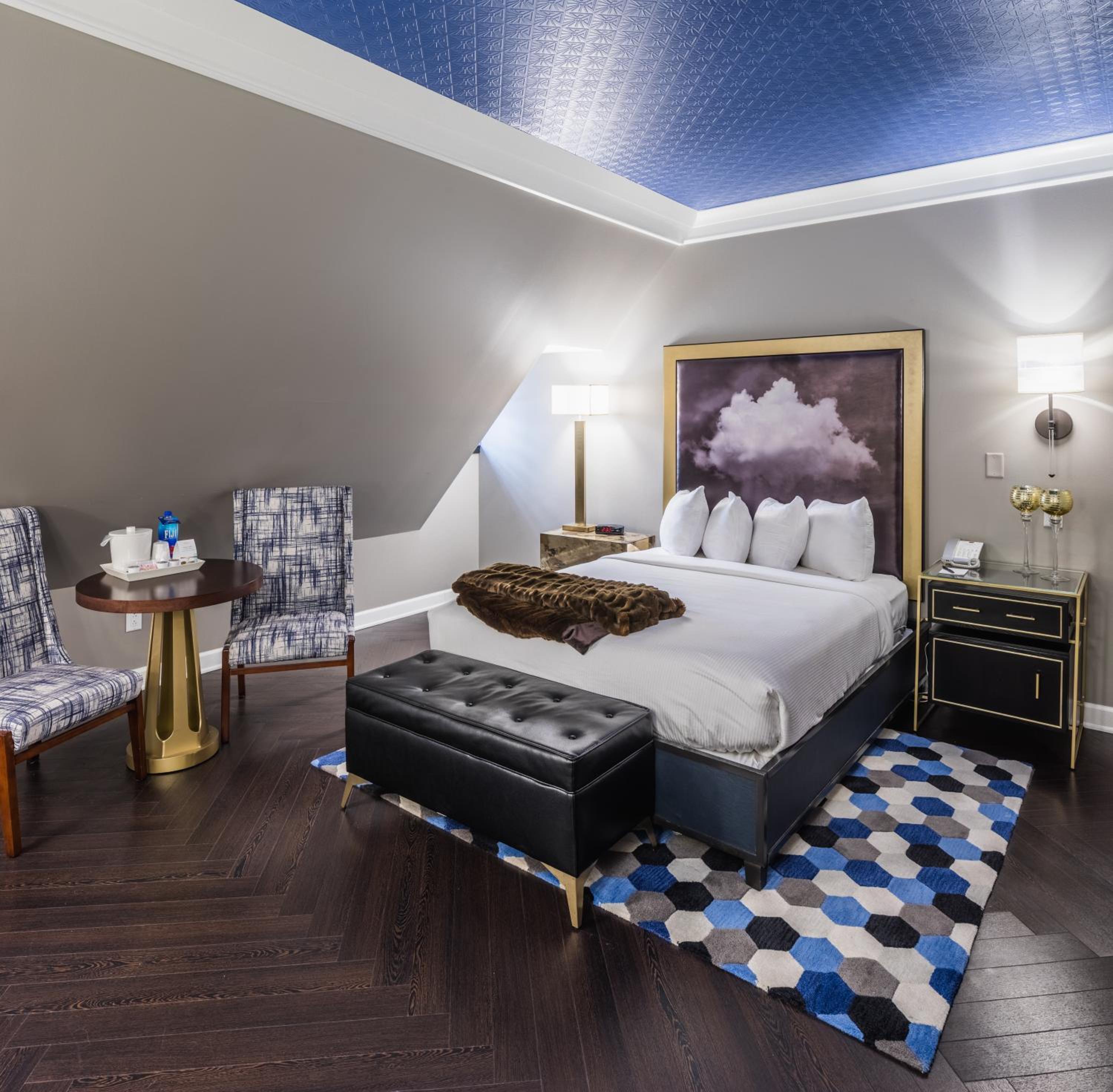 A bedroom beneath a sloped ceiling with dark wood herringbone flooring, a bed, and blue patterned accents.