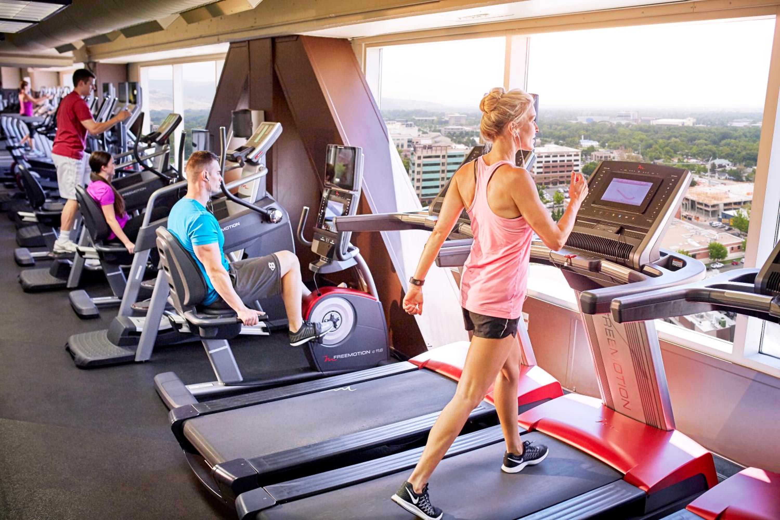Hotel gym with exercise equipment facing panoramic windows overlooking the city.