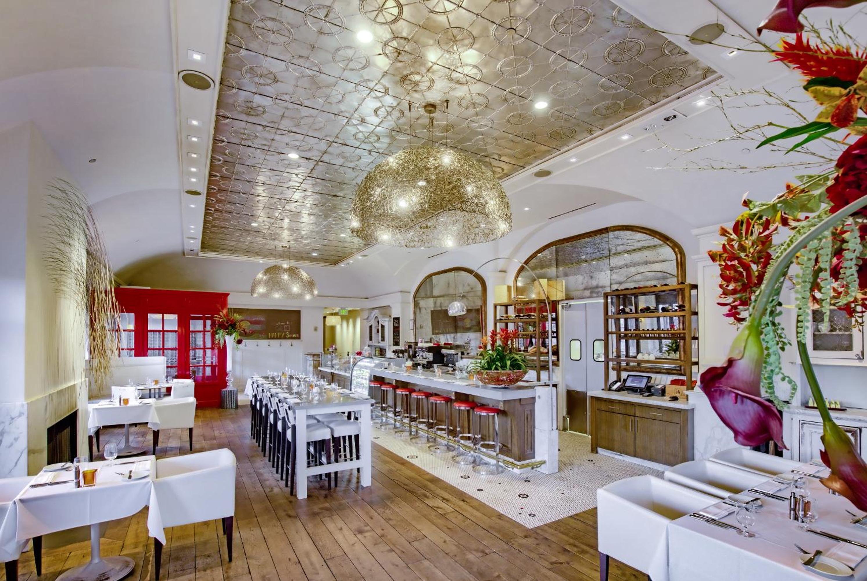 Restaurant dining room with a pressed-tin ceiling, woven pendant chandeliers, and a marble bar counter.