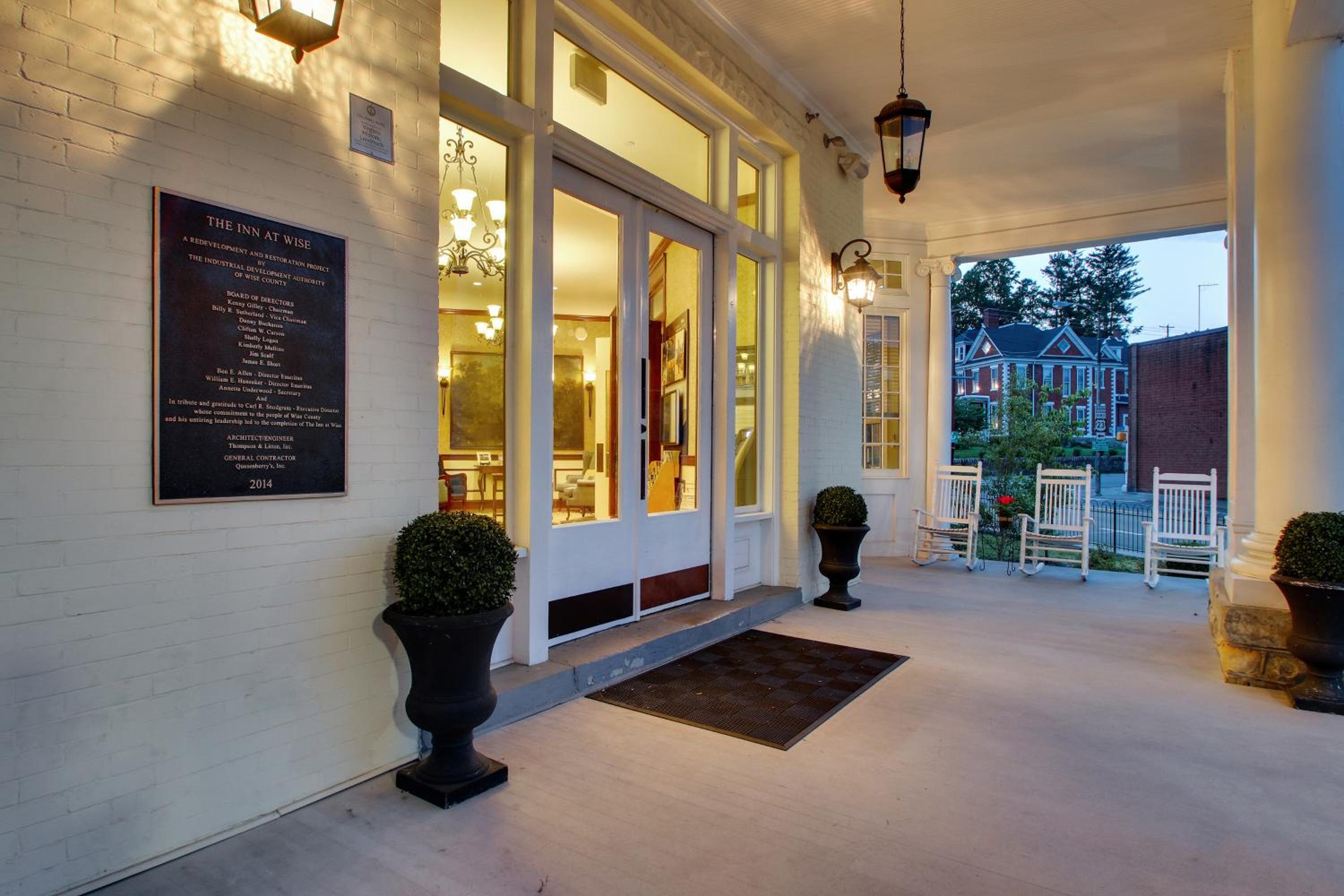 A covered front porch with white columns, hanging lantern lights, rocking chairs, and glass entrance doors.