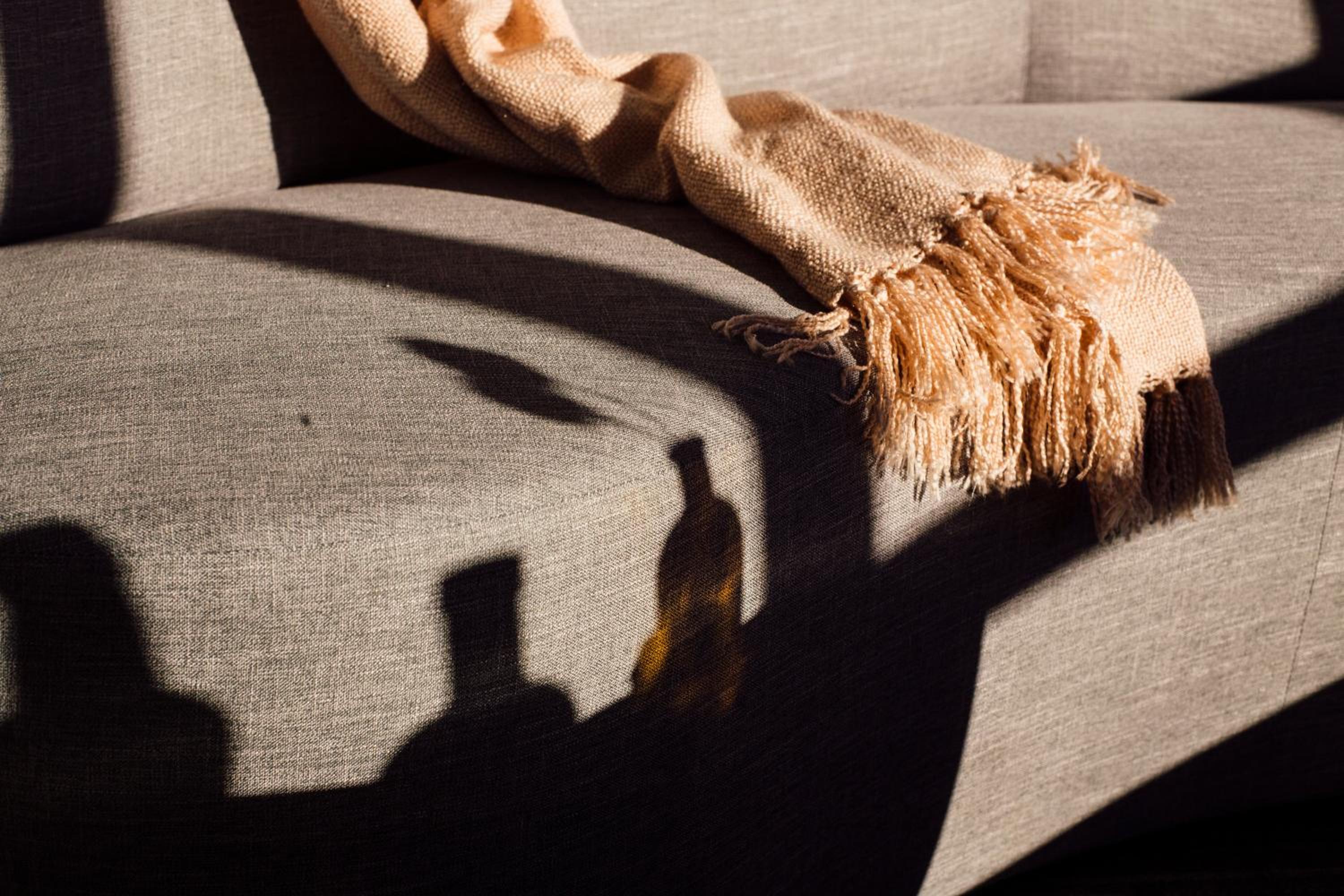 Shadows of glass bottles fall across a textured sofa draped with a fringed woven throw blanket.