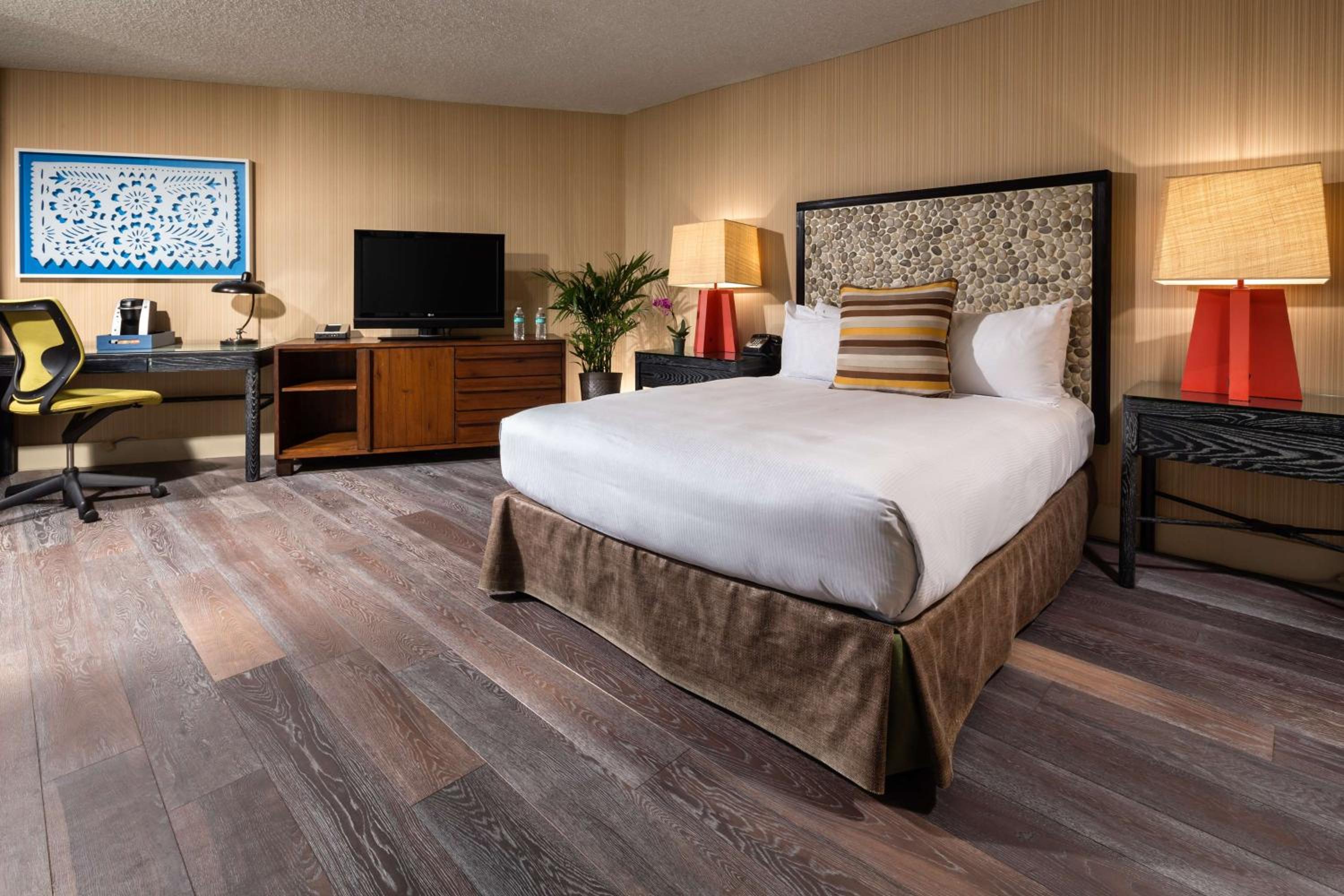 A bedroom with a pebble headboard, bedside lamps, wood-grain flooring, and a work desk.