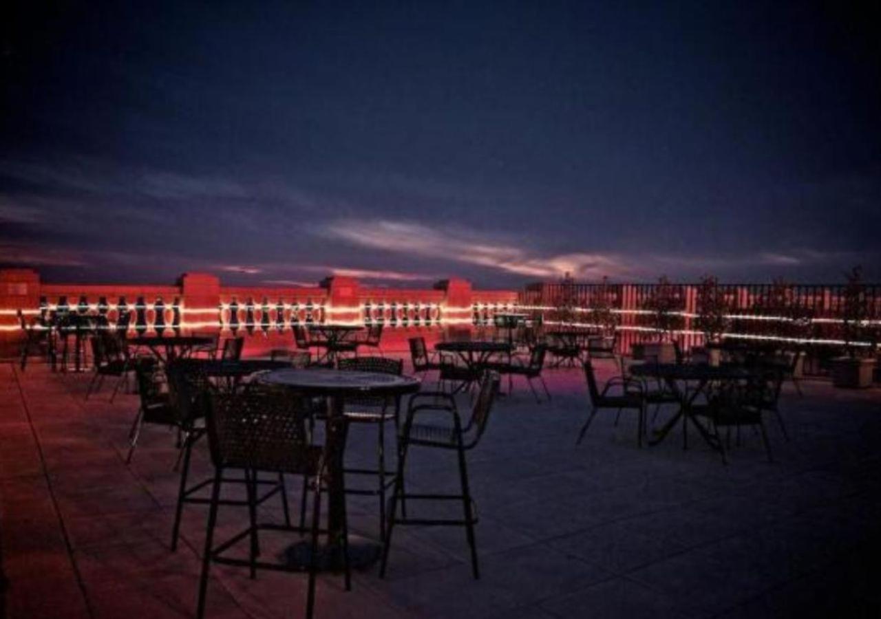A rooftop terrace at dusk with high-top tables, bar stools, and neon red lighting along the balustrade.