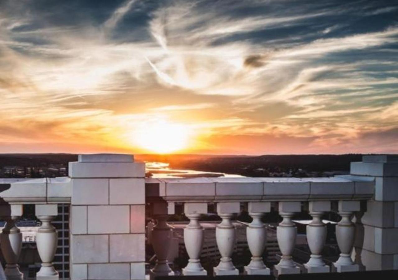 A white stone balustrade on a rooftop overlooking a river and distant hills at sunset.