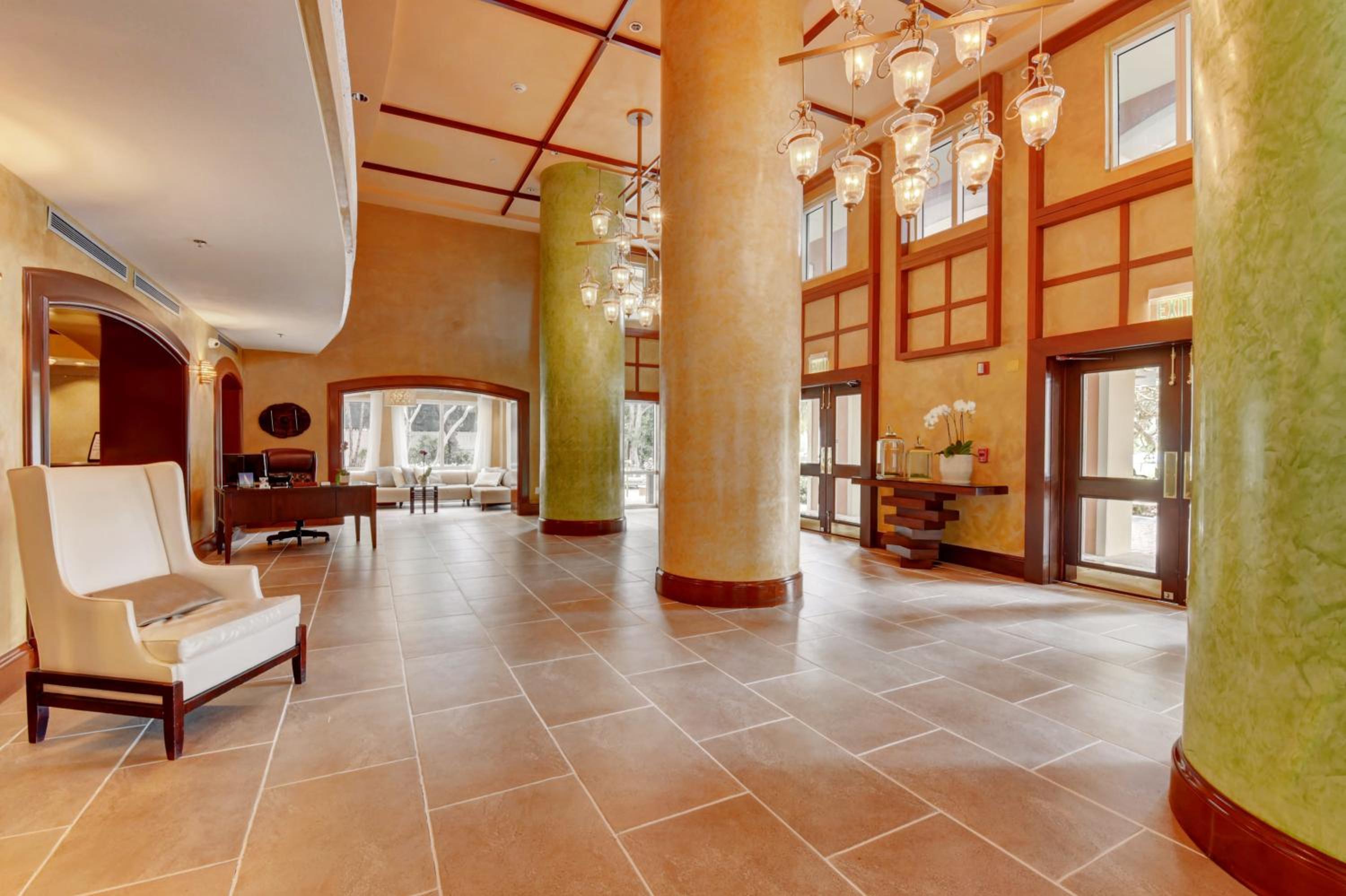 Spacious hotel lobby with large textured columns, tiled flooring, hanging chandeliers, and high ceilings.