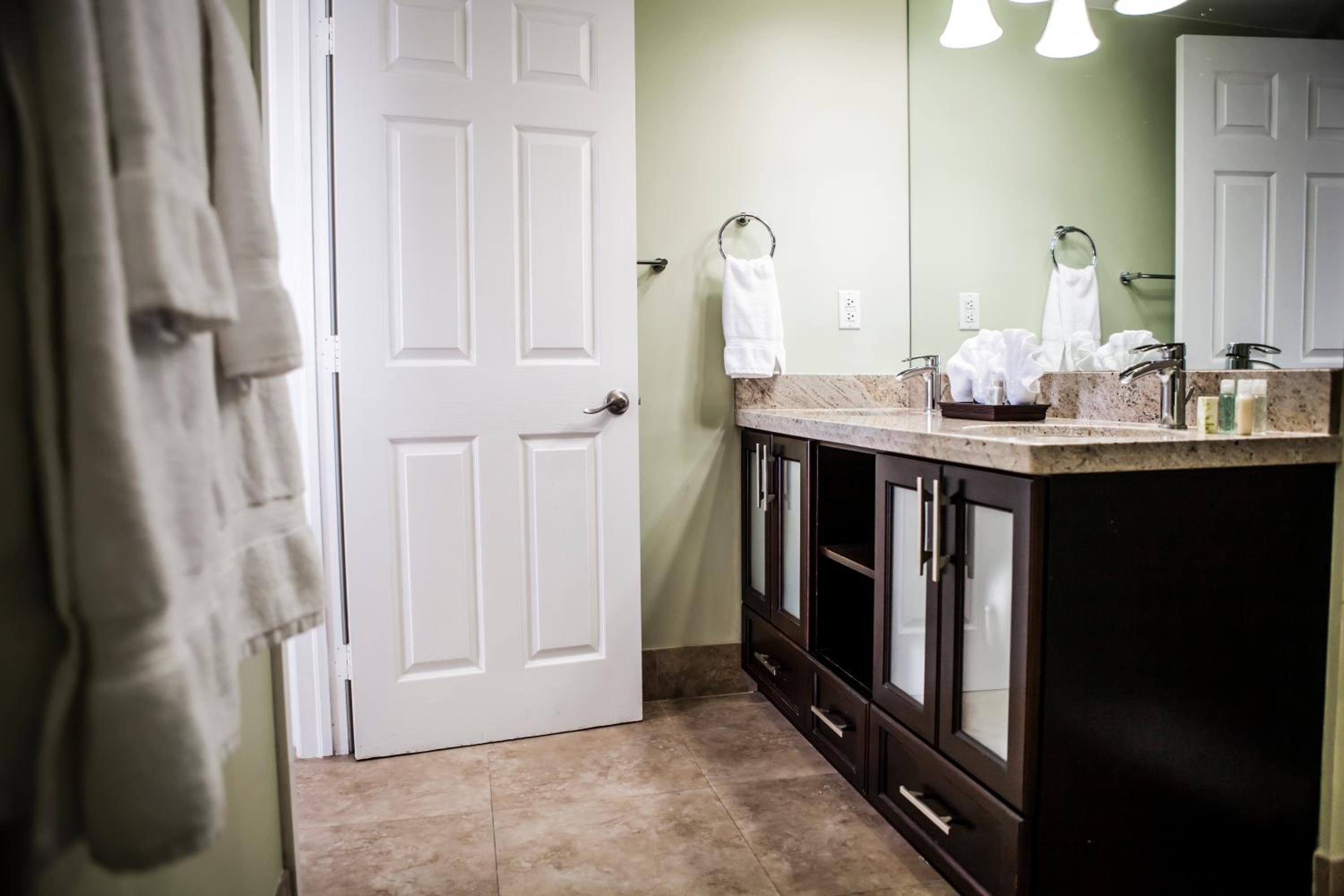 Bathroom with a dark wood vanity, stone countertop, sinks, and an open white door.