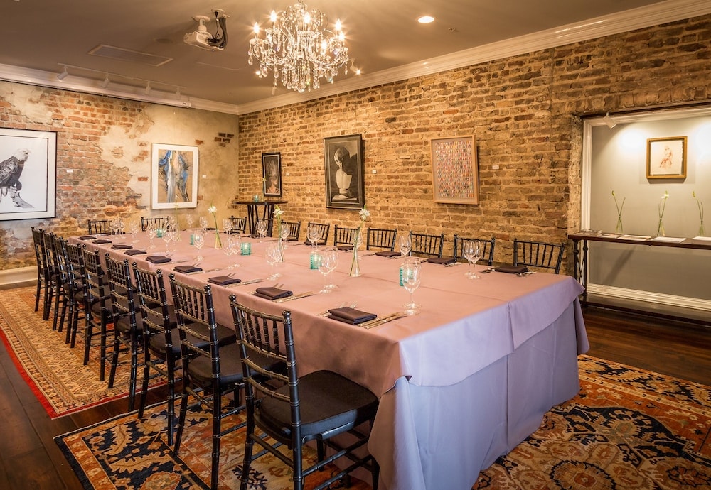 A long dining table set with glasses and linens inside an event room with exposed brick walls and an ornate chandelier.