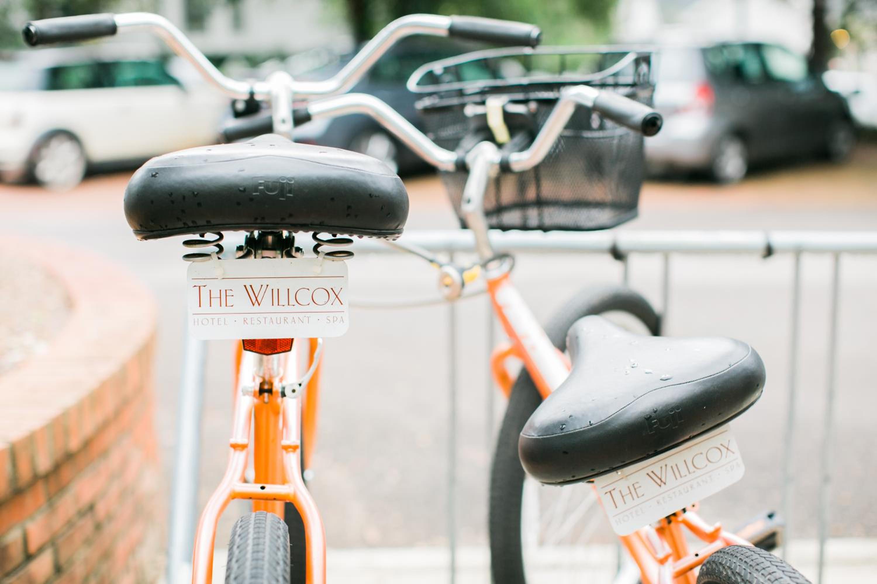 Close-up of orange cruiser bicycles parked on a street rack, bearing branded license plates beneath the seats.