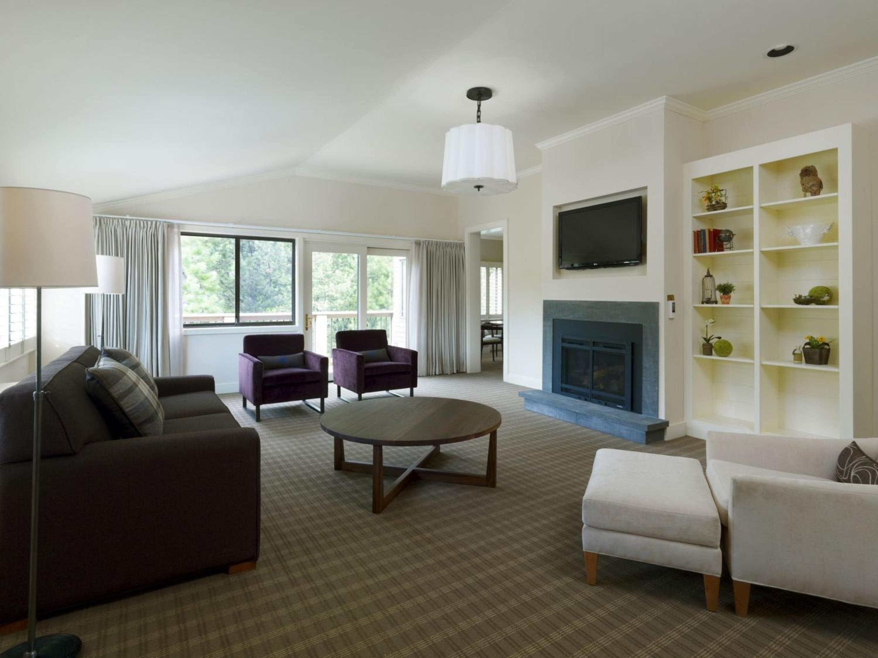 A living room with a fireplace, television, round wooden coffee table, armchairs, and plaid carpeting.
