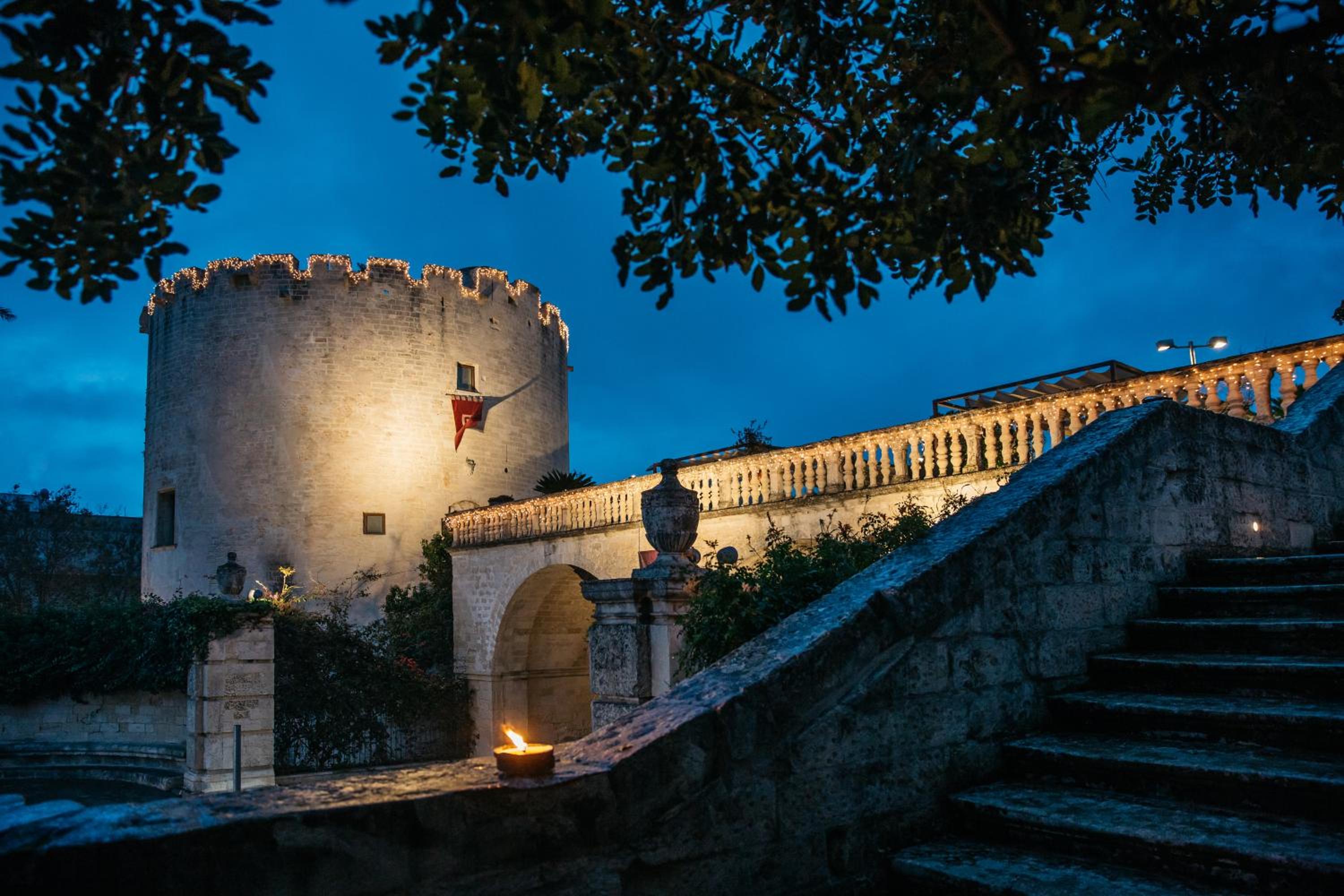 Illuminated stone tower and balustrade staircase of Torre Del Parco against a deep blue evening sky.