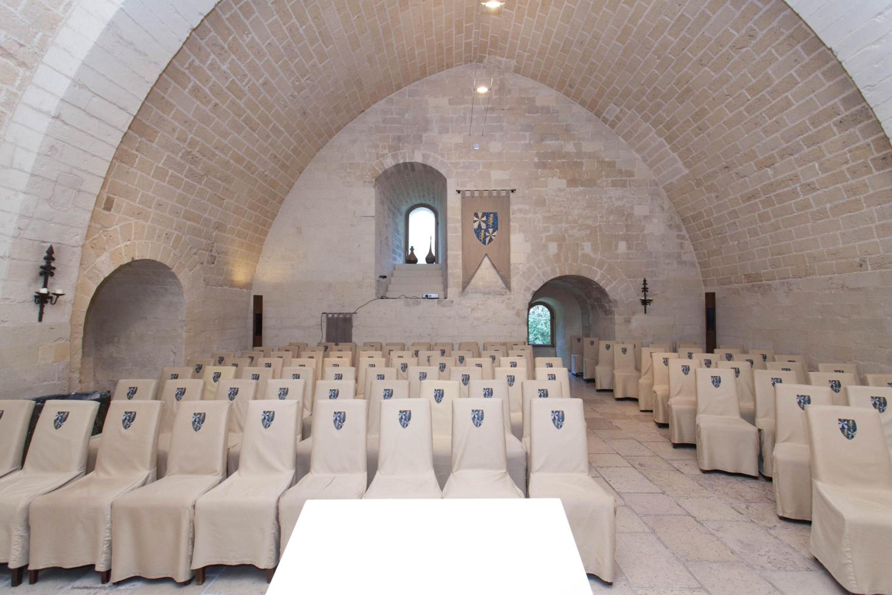 Vaulted stone room with rows of slipcovered chairs facing a lectern beneath a high pointed arch.
