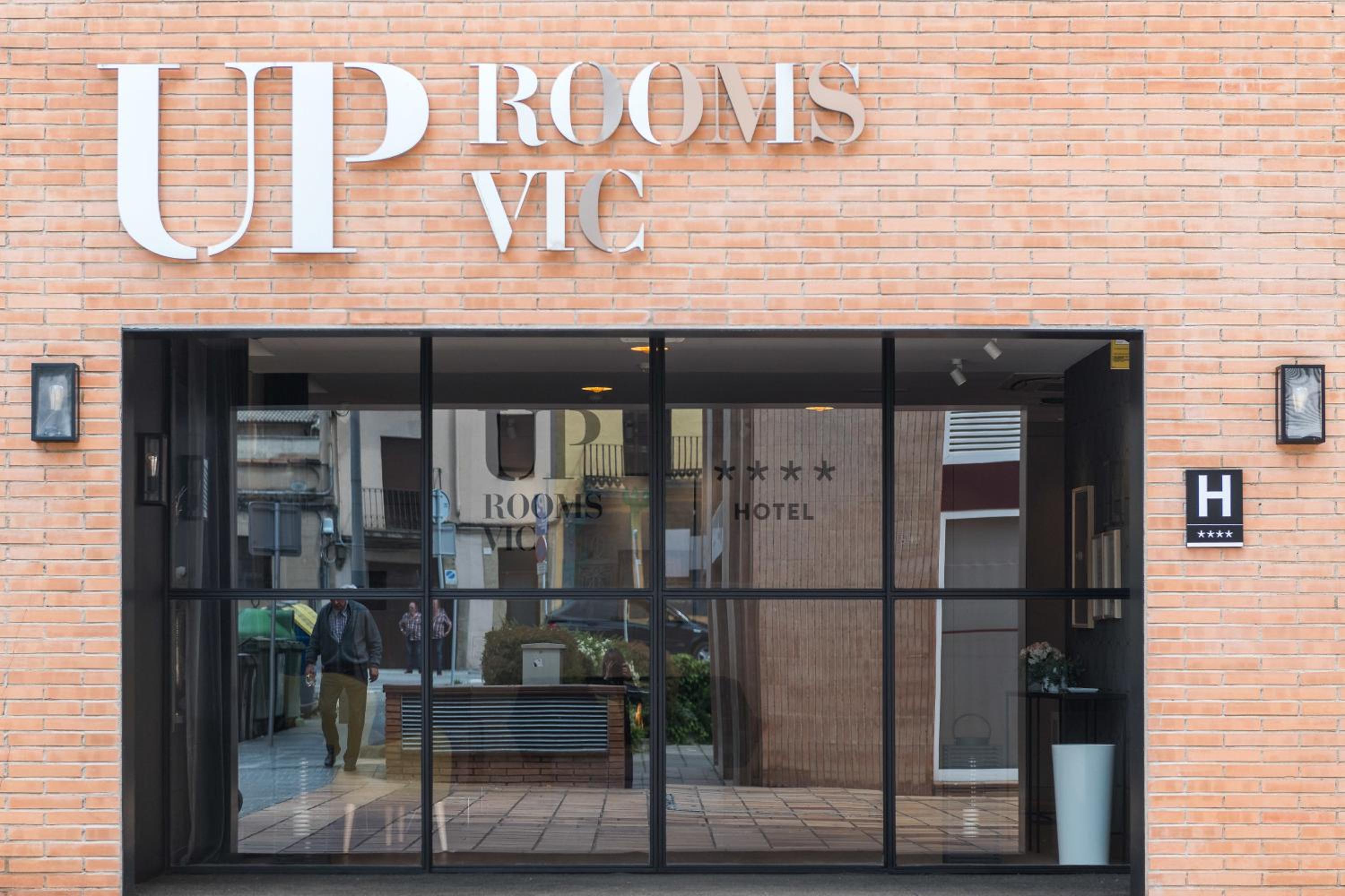 The brick facade and glass street entrance of Up Rooms Vic Hotel.