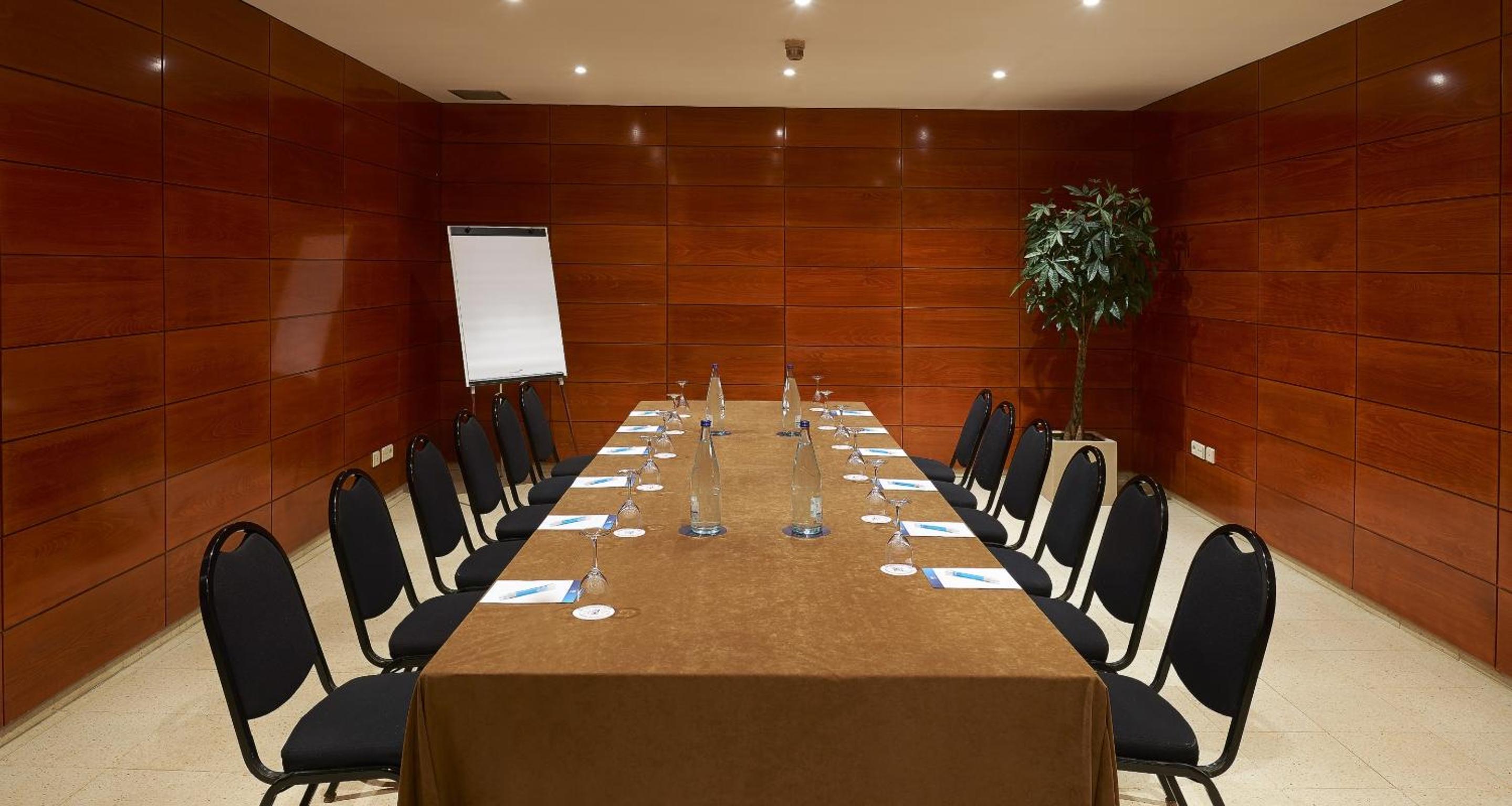A conference room with polished wood wall panels, a long clothed table, chairs, and a whiteboard.