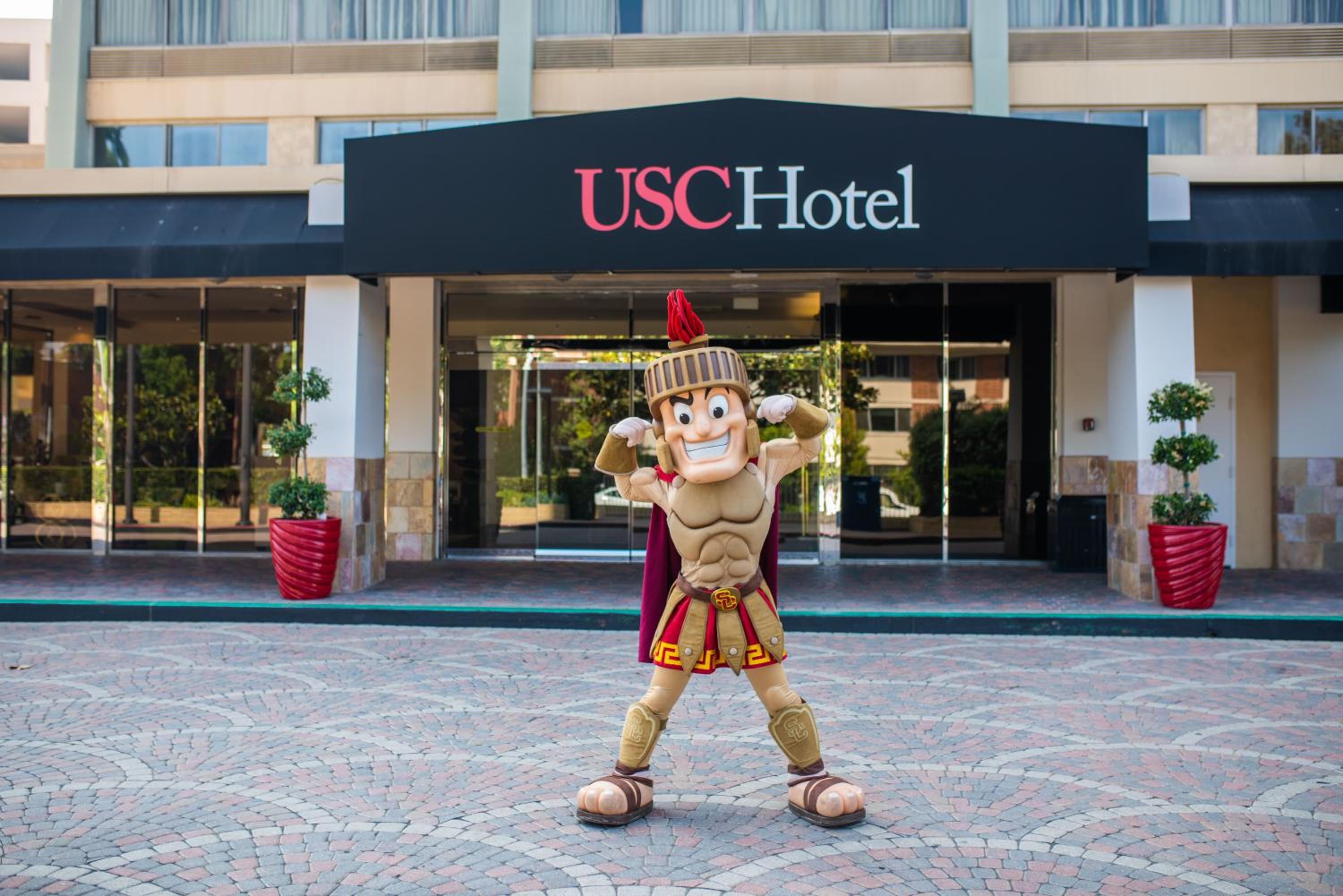 The USC Trojan mascot in full armor costume posing in front of the hotel entrance.