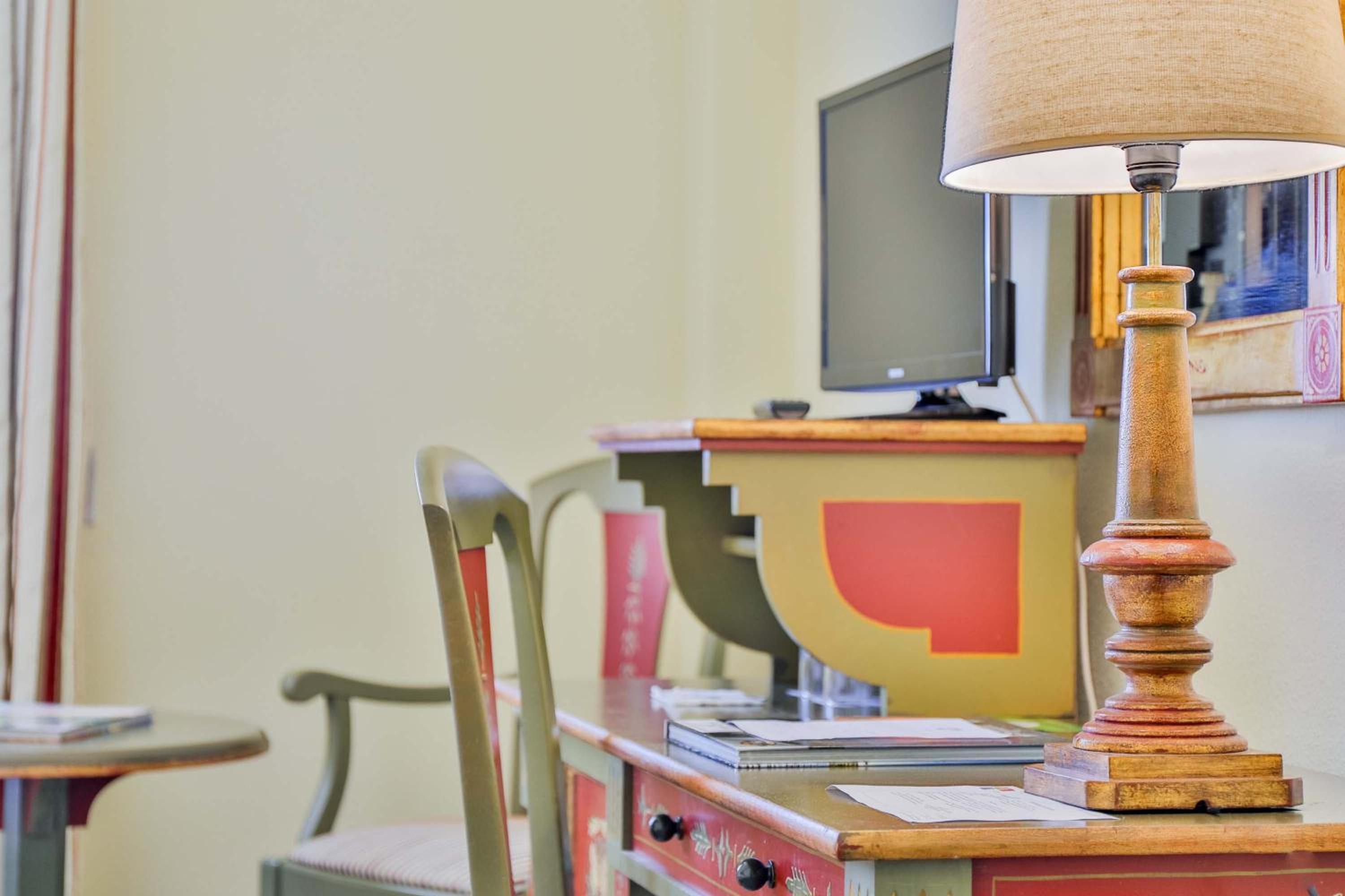 A wooden desk with green and red trim, topped by a turned lamp and papers, beside a matching chair.