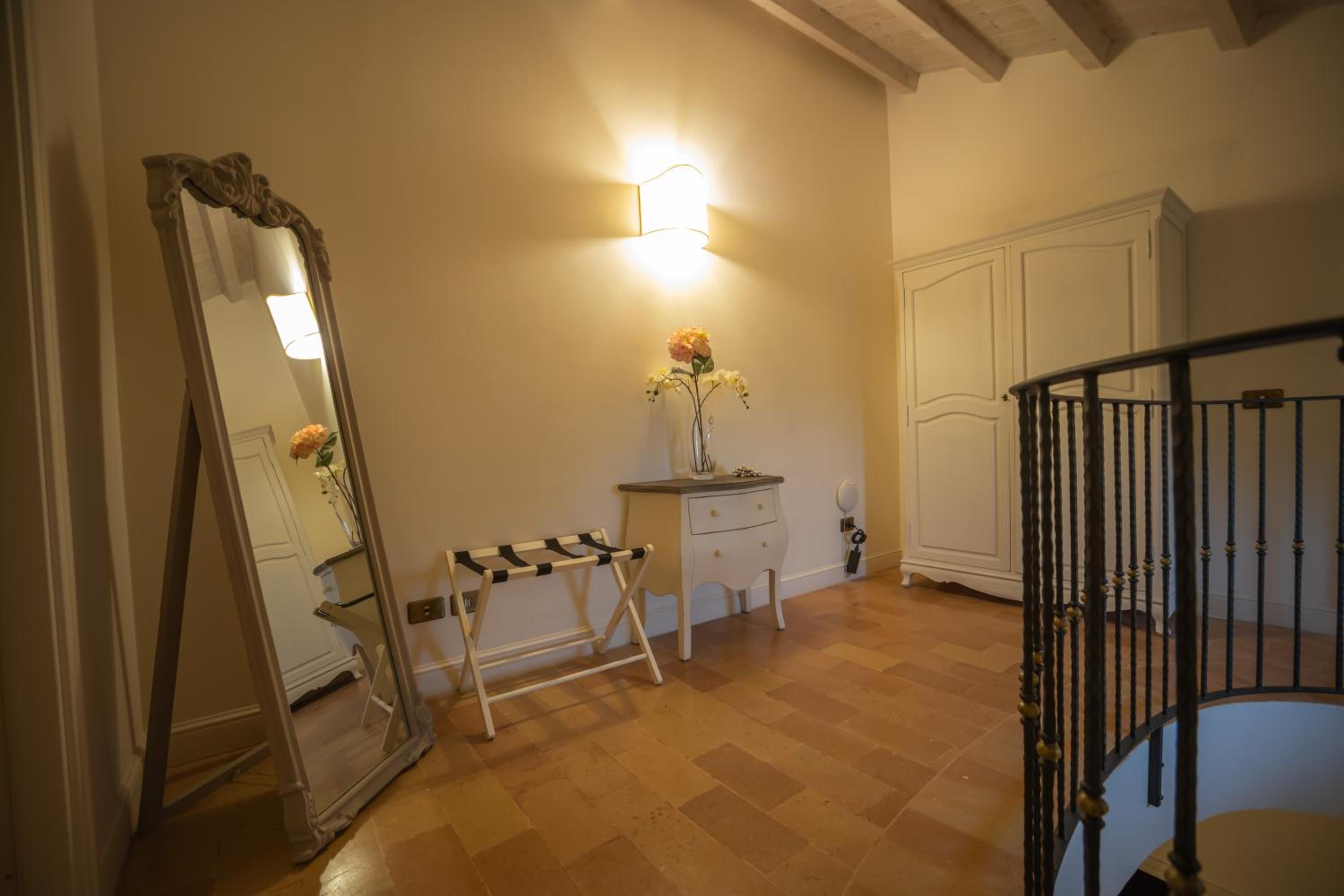 Hallway with terracotta tile flooring, a tall wooden-framed standing mirror, an arched armoire, and stair railing.