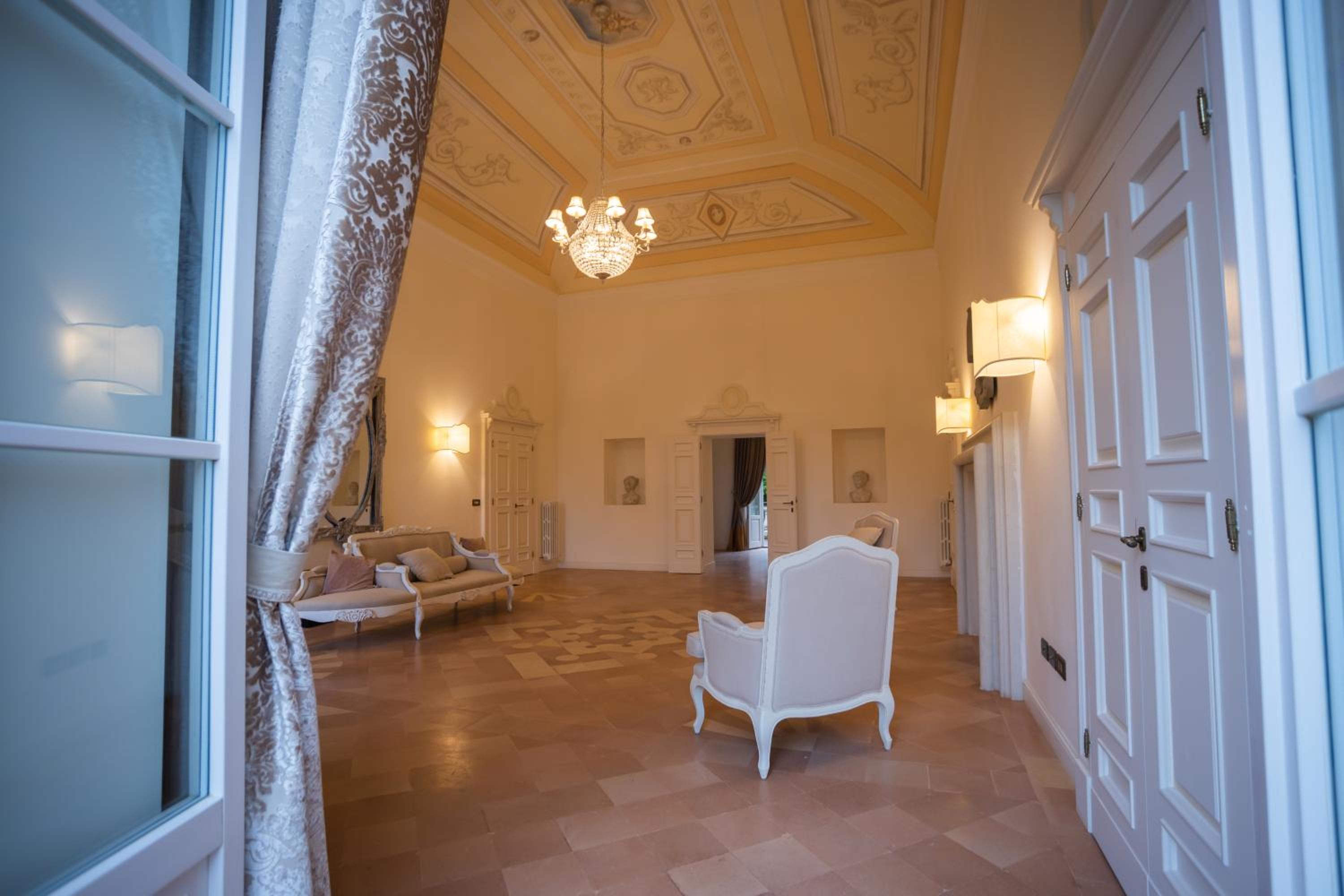 A grand salon with a painted vaulted ceiling, crystal chandelier, tiled floor, and vintage armchairs.