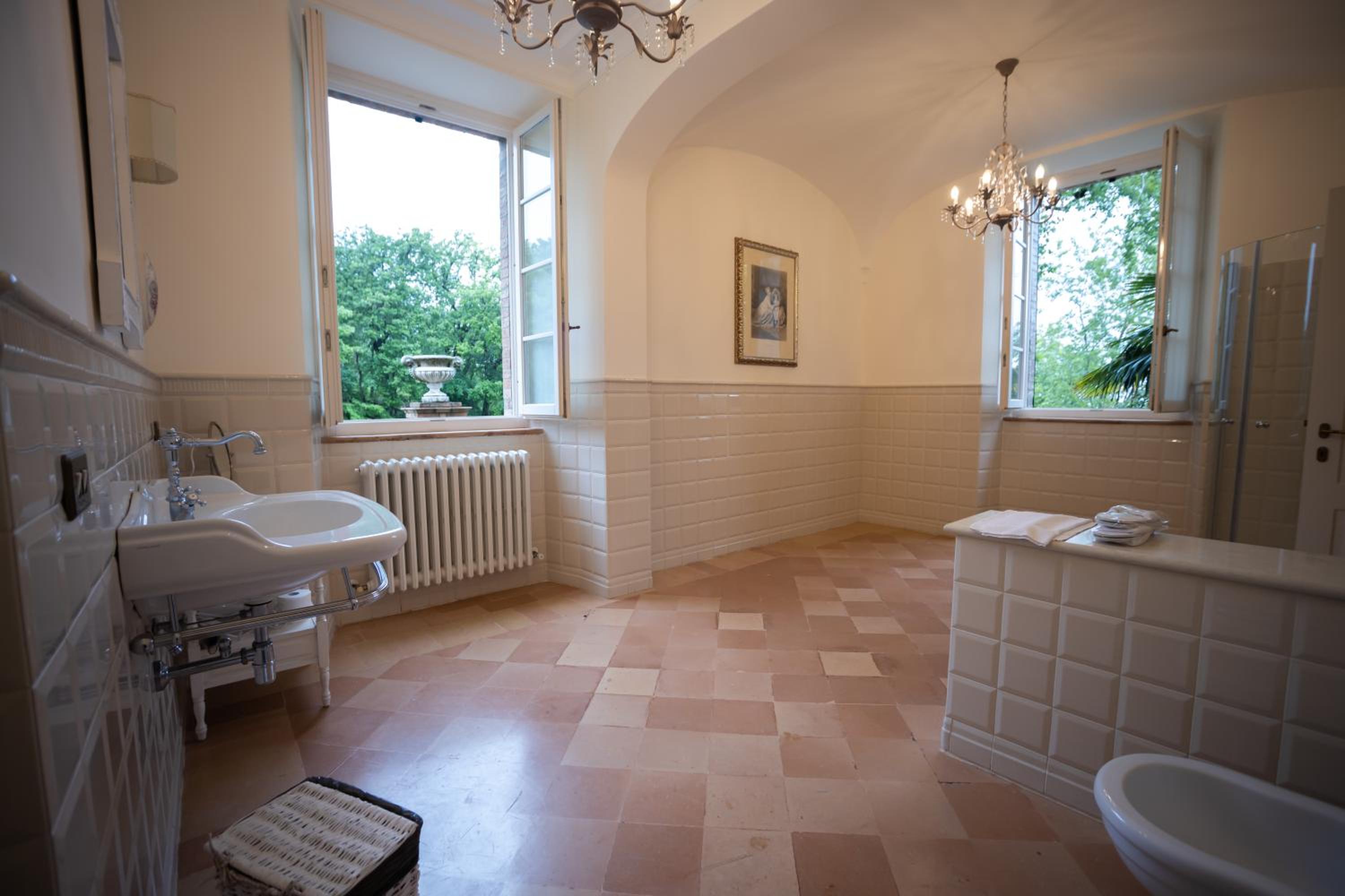 Spacious bathroom with tiled walls, terracotta flooring, a pedestal sink, radiator, and large open windows.